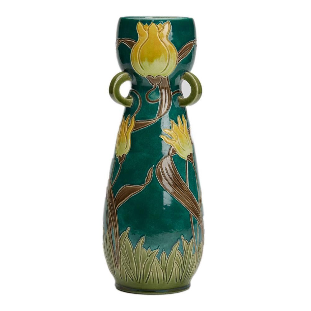 A stunning Art Nouveau Burmantofts Faience vase of tall elegant form with three small loop handles below a cup shaped top, the body decorated incised tube-lined style tulips in yellow brown and green on a bottle green ground. The vase is numbered