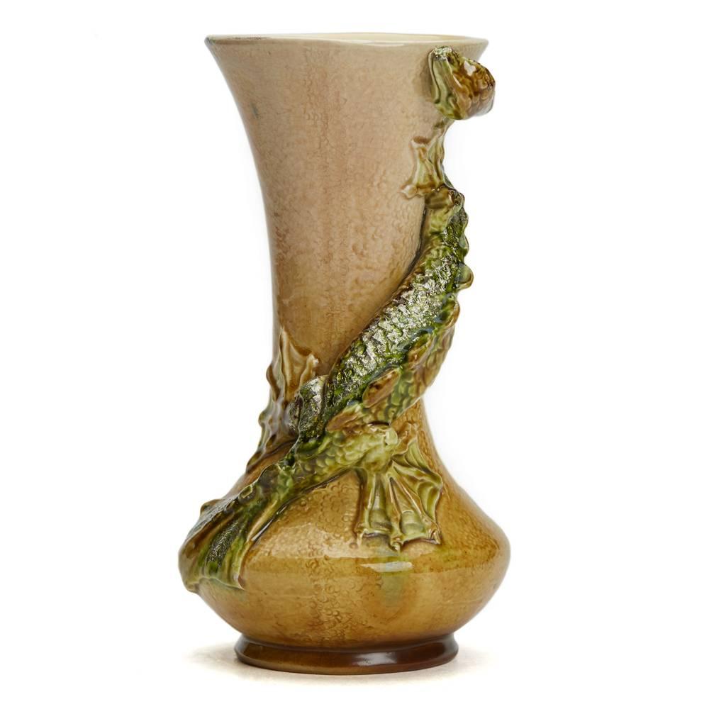 A rare Burmantofts Faience Dragon vase of waisted cylindrical form applied with a dragon-like grotesque creature, glazed brown and green and highlighted with gilt aventurine on a sand yellow ground. The vase is numbered 616 and has impressed marks