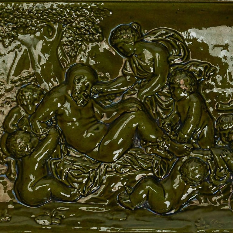 A scarce Burmantofts Faience Bacchanalian tile of rectangular form modelled in relief with figures attending to a resting man set within a raised stepped edge and decorated in green glazes. Incised Burmantofts marks along with Wilcock & Co Leeds