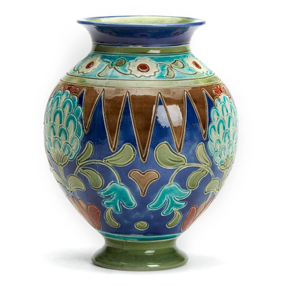 An impressive Burmantofts Faience Partie-color vase decorated with artichoke shaped flowers in Persian style with a rounded bulbous body on a narrow rounded pedestal foot and everted rim. The vase is painted brown, green, red and white on a blue