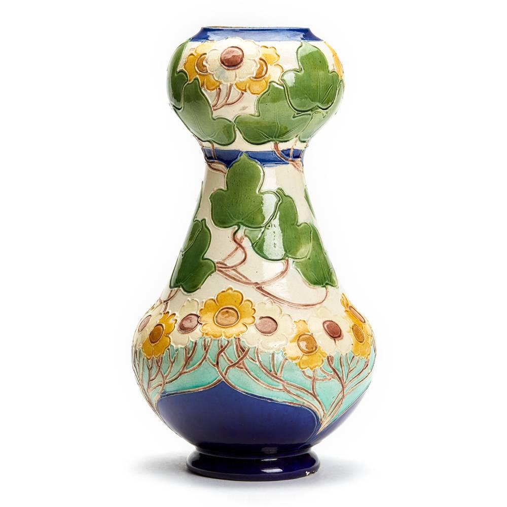 A Burmantofts faience Partie-Colour vase designed by Joseph Walmsley with a swollen with tapering neck with swollen rim, modelled in low relief with trailing flowers and foliage, painted in shades of blue, green, yellow and turquoise on a cream