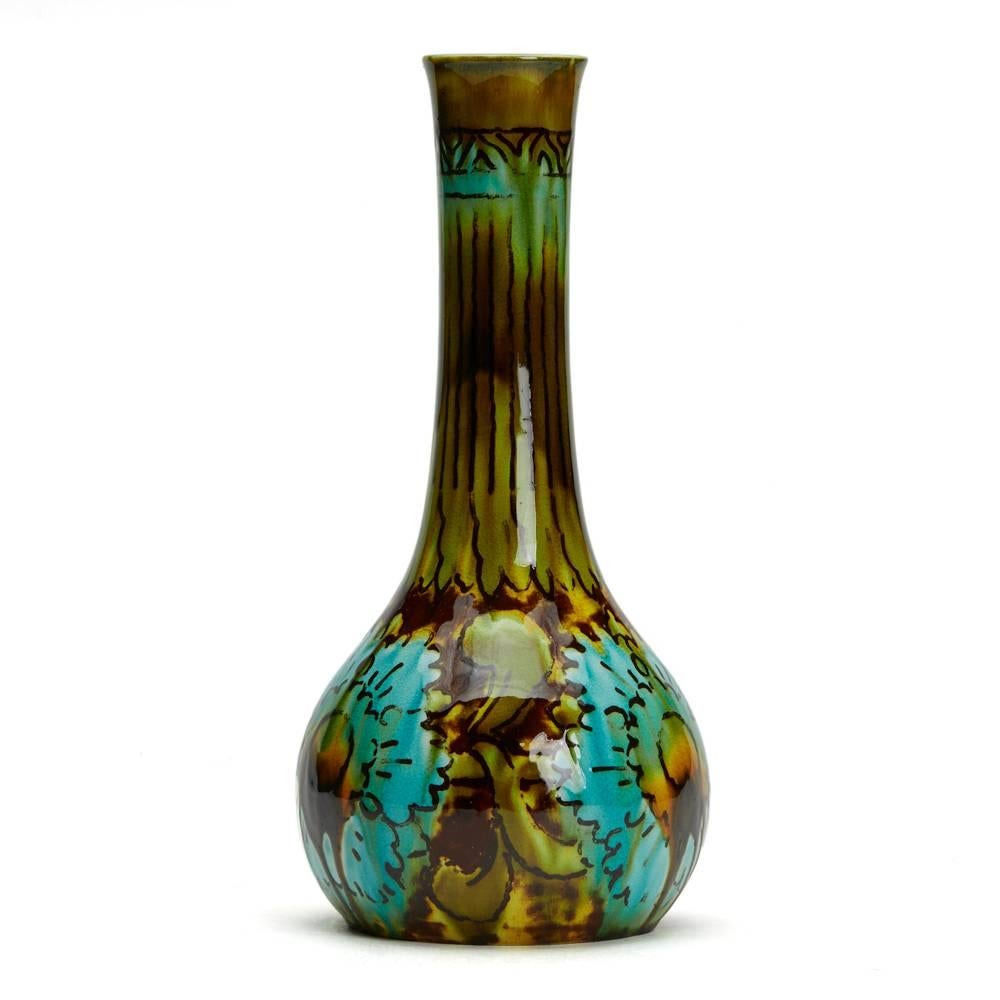 An unusual Burmantofts Faience Barbotine bottle vase painted with stylised floral designs in shades of green, brown and turquoise blue with a tall slender neck. The vase is marked model no.1528 and has impressed makers marks to the