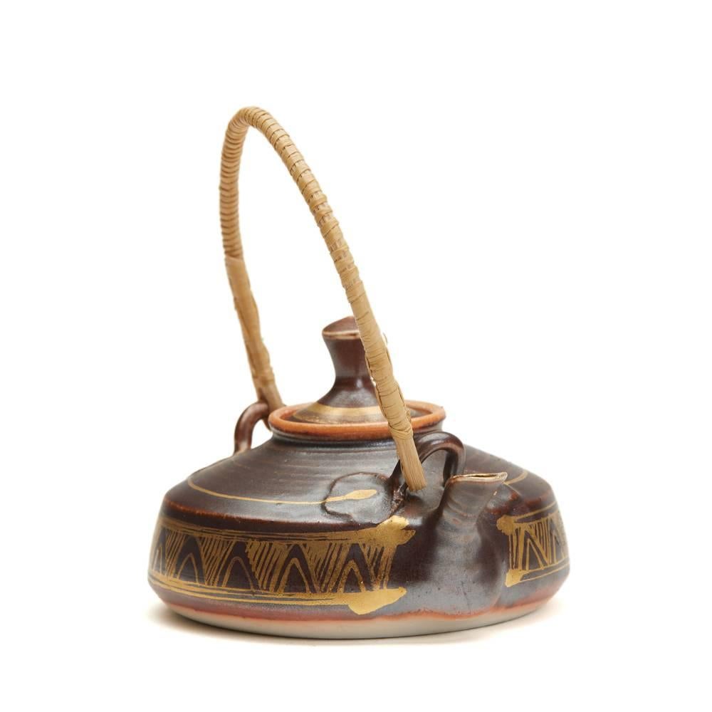 A very fine and stylish Studio Pottery miniature teapot of squat rounded form with a woven cane handle and finely decorated in metallic brown glazes over decorated with gilded patterns, the short squat pouring spout with a gilded rim. The teapot has