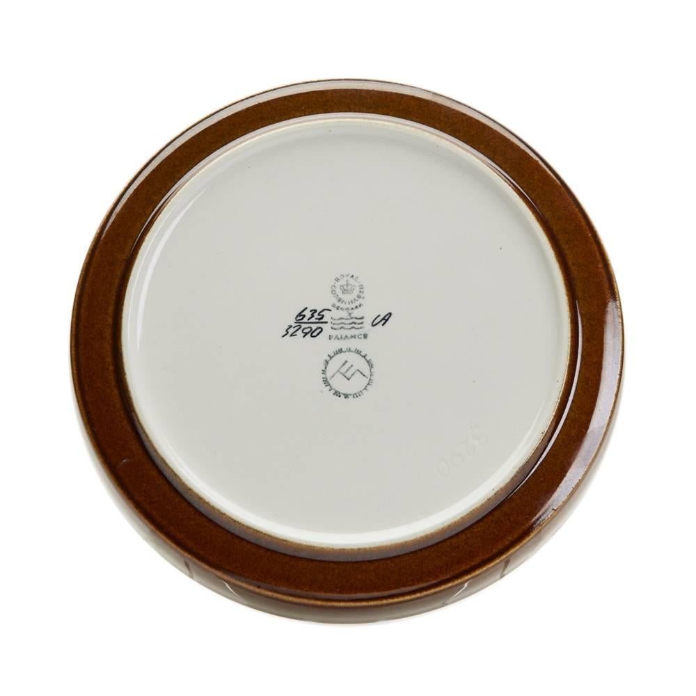 A stylish Royal Copenhagen faience dish designed by Ellen Malmer of shallow rounded form the centre decorated with stylized stems with buds in yellow and brown glazes on a white ground with brown glazes around the outer edge. The dish has printed