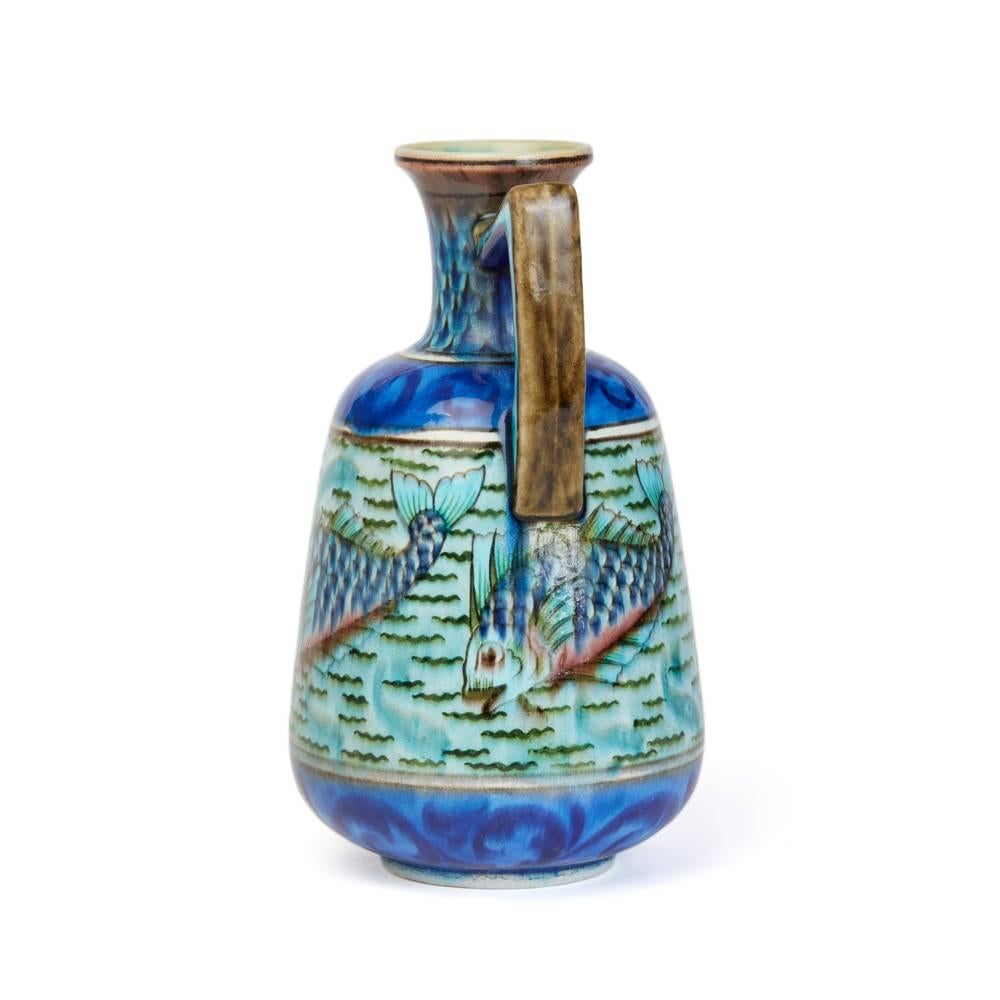 A rare Burmantofts Faience Anglo-Persian design single handled art pottery vase painted with a frieze of scaly fish swimming in a rippling river. Hand-painted in shades of turquoise, blue, green and brown between two bands of blue scroll foliage.