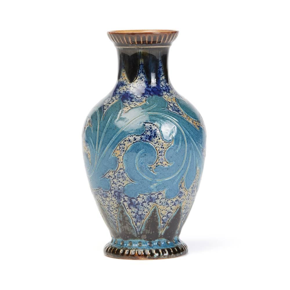 An unusual Doulton Lambeth art pottery vase by Arthur Barlow decorated with incised scrolling acanthus leaves painted in shades of blue on a stipple patterned ground in blue and salt glazed patterns with leaf borders around the top and bottom edges.