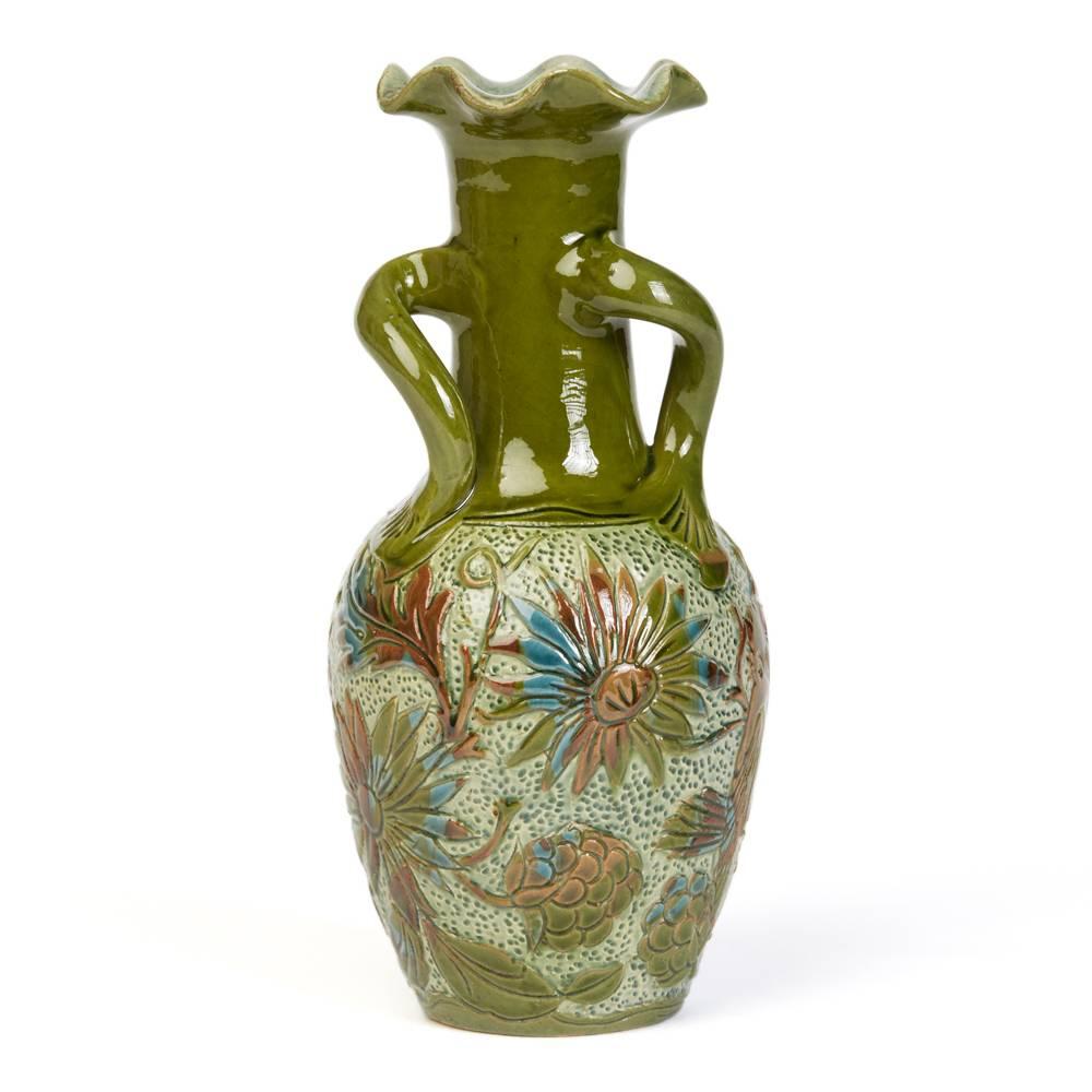 A stylish Alexander Lauder art pottery three handled vase of slender bottle shape, the body decorated in sgraffito pattern with birds set amidst flowering shrubs. The vase has scrolling handles and folded back fluted rimmed top and is hand-painted