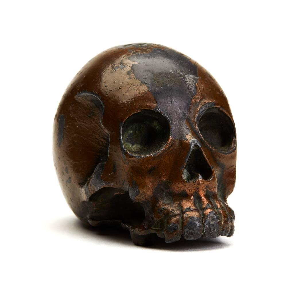 An antique Japanese Meiji lacquered antimony Okimono modelled as a naturalistic human skull with a lacquered brown finish and traces of gilding to the base. The heavily made skull is well proportioned and has a raised seal signature mark to the