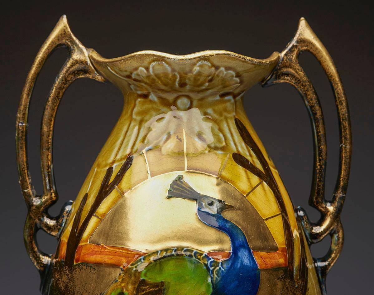 An Art Nouveau Thomas Forester twin handled art pottery vase decorated with a tubelined peacock design vase hand painted in richly glazed colours with rich gilding. The vase has ornate open work handles to either side of the neck and has an