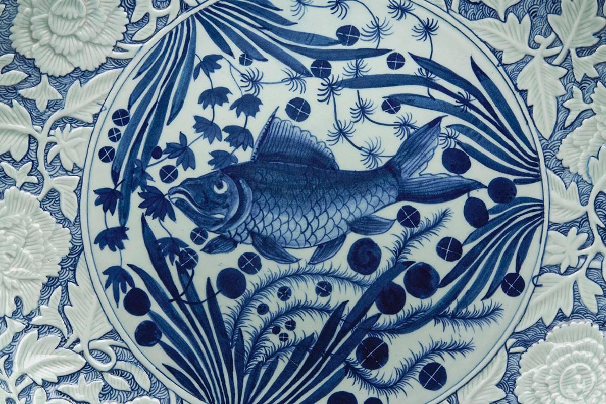 A large and impressive Chinese blue and white charger of shallow bowl form, the centre decorated with a large fish swimming amidst pond weed and set within a low relief moulded rim with flowering prunus with a relief trailing floral  moulded shaped