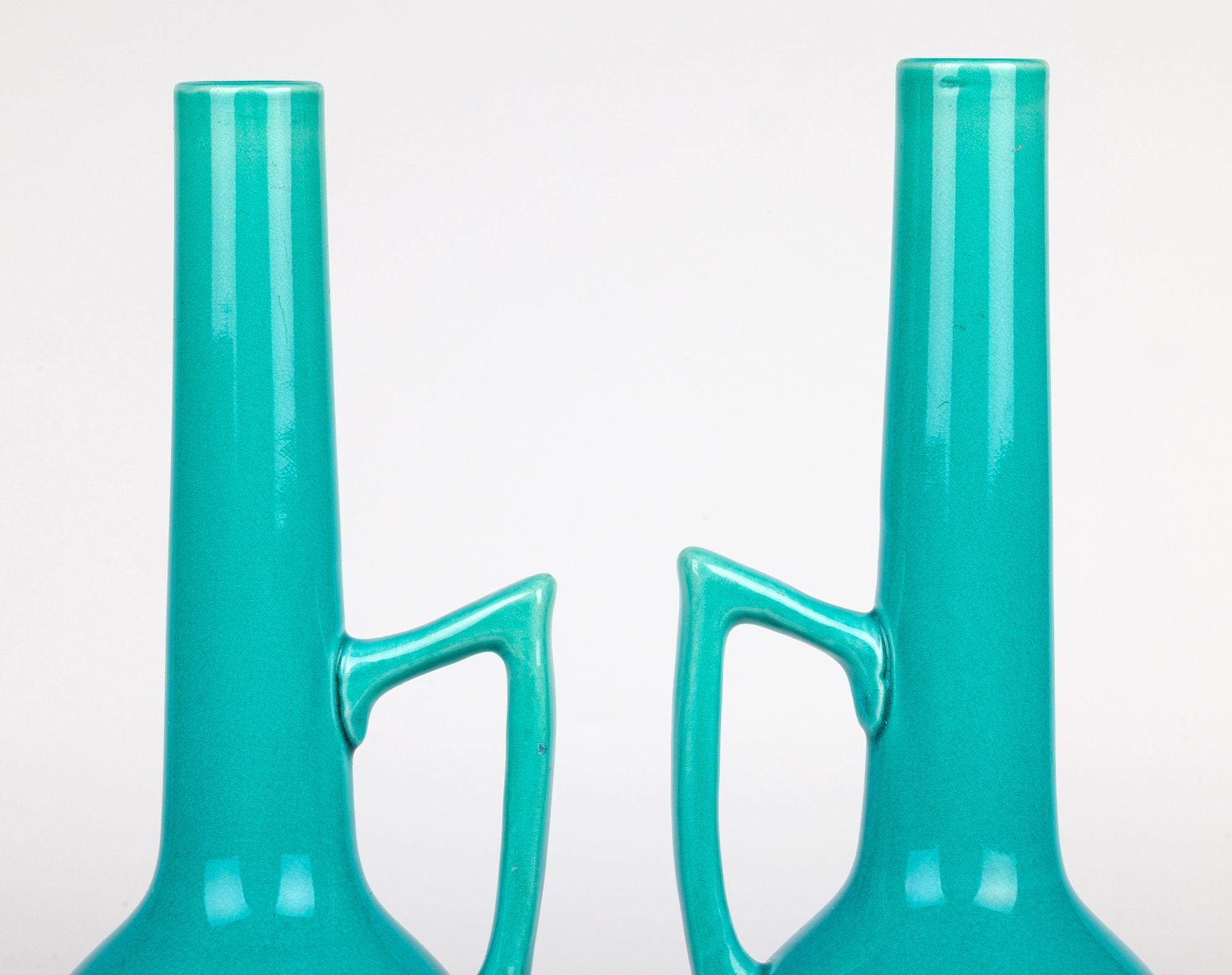 A rare and elegant pair Burmantofts Faience art pottery handled ewer shaped vases decorated in turquoise glazes and dating from around 1890. These stunning earthenware vases stand raised on a small narrow round pedestal foot with an egg-shaped body