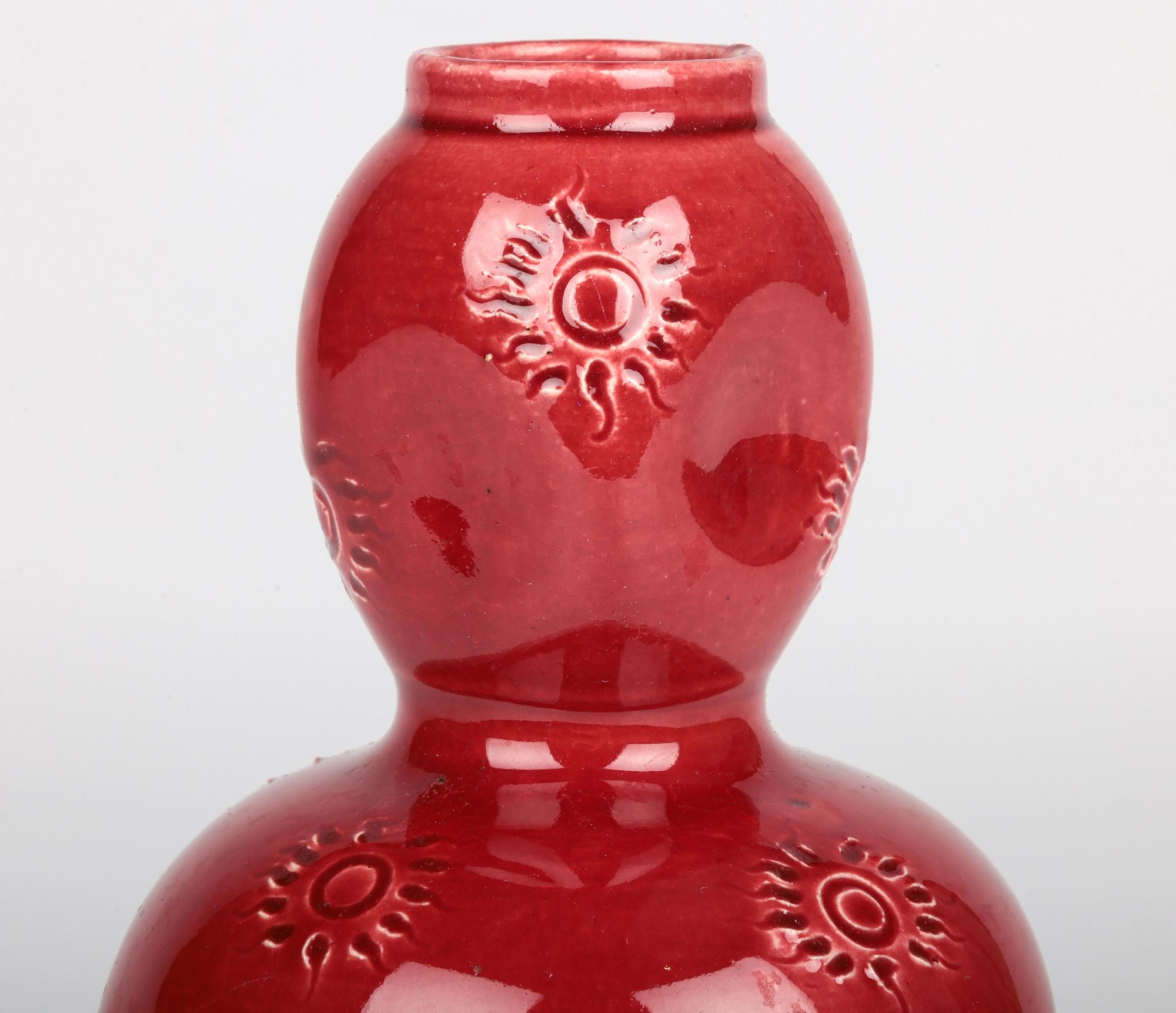 An unusual and stylish Burmantofts Faience art pottery double gourd vase decorated with sun burst patterning and decorated in red glazes and dating from around 1890. This stunning lightly potted earthenware vase stands raised on a narrow round