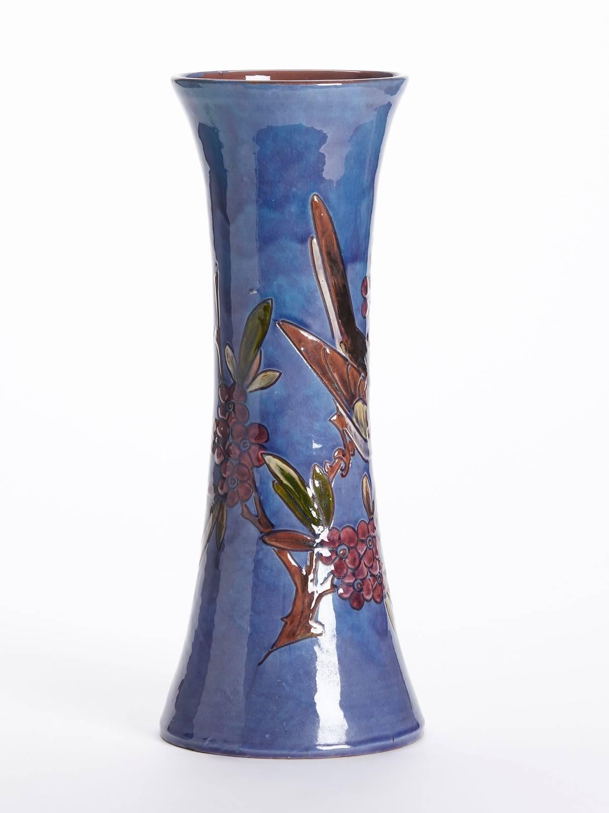 An unusual art pottery vase of trumpet shape decorated with a bird perched on a fruiting branch by William Baron. The tall waisted vase is incised and hand decorated and incised with a garden bird perched on a branch with berries painted in colours