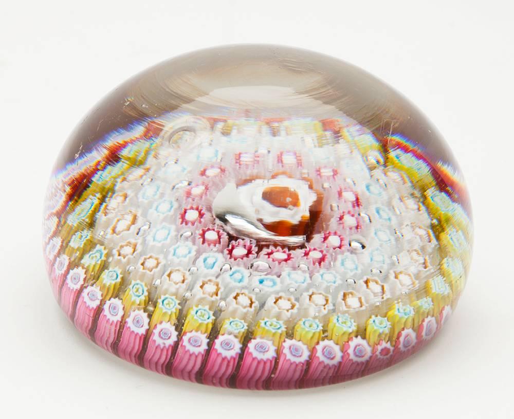 A stunning English concentric glass paperweight with five rows of cog style canes surrounding a central larger cane. The canes are of various colours and set within a clear glass body. The base of the paperweight is well-finished with an outer foot