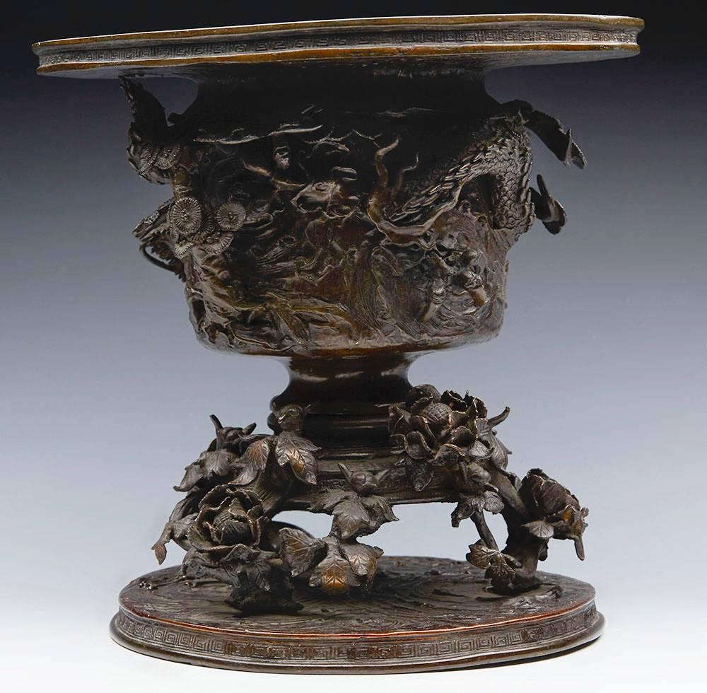 A superb antique Japanese Meiji Bronze Usubata (vessel for traditional flower arranging) applied with a scrolling dragon amidst fir like shrubs with prunus floral designs to the base dating from the 19th century. The Usubata comes in two parts with