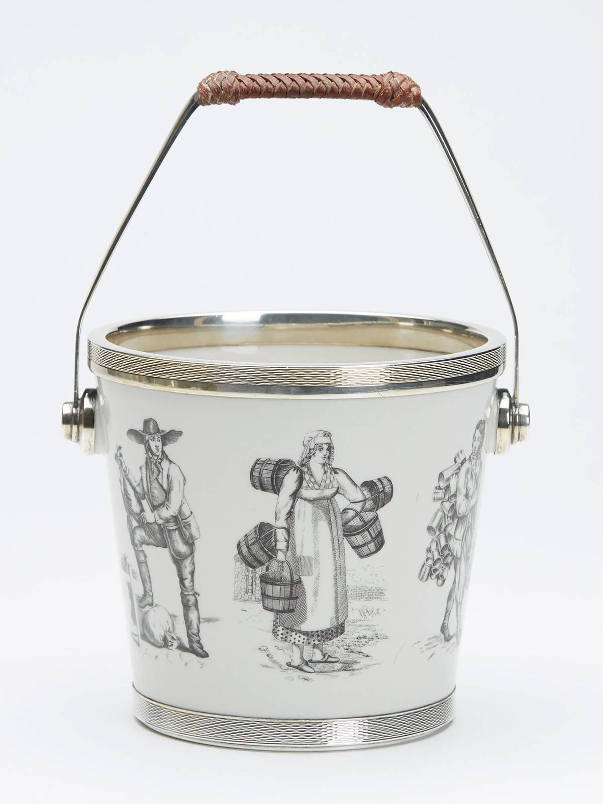 A vintage silver mounted bucket shaped ceramic ice bucket decorated with continental style figures in black on a white ground. Believed to be Scandinavian the ice bucket has silver rims to the foot and top and is fitted with a silver swing handle