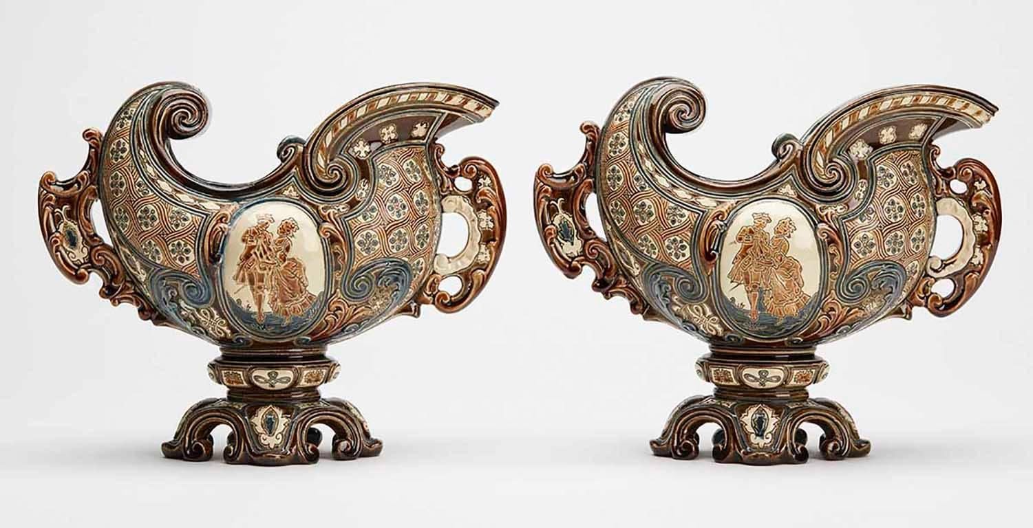 A stylish pair of antique Bohemian Majolica console bowls or vases elaborately decorated by Gerbing & Stephan. The earthenware bowls Stand raised on a narrow pedestal foot with helmet shaped bodies with central panels with incised courting figures