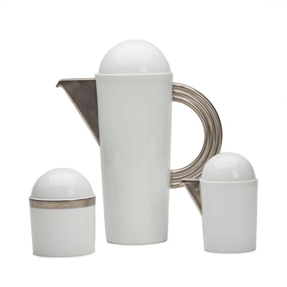 A stunning and stylish vintage Rosenthal porcelain three-piece coffee set designed by Mario Bellini and comprising of a tall elegant coffee pot with silver spout and flat rainbow styled handle with domed cover, a sugar bowl with a silver line design
