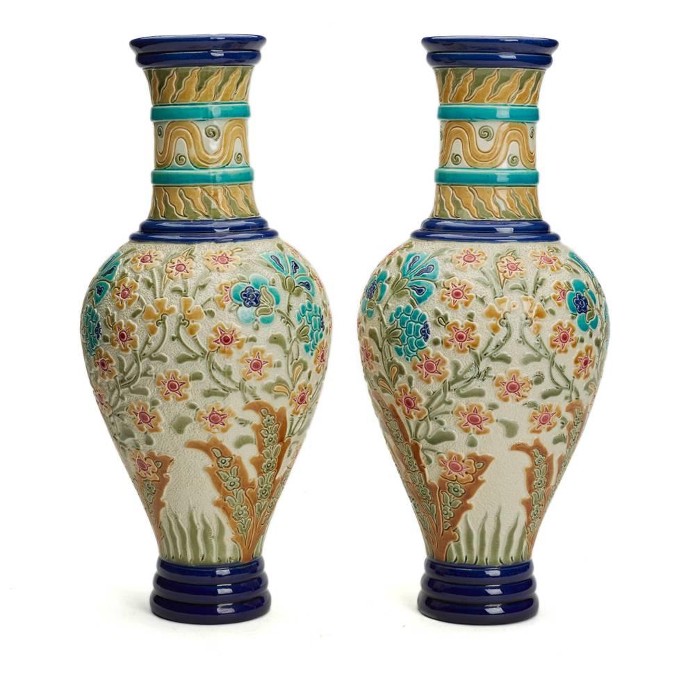 A stunning pair of Burmantofts Faience vases of slender baluster form, cast in low relief with flowers and foliage, in shades of blue, turquoise, green, yellow and red on a cream ground. The vase is marked Col No. 112 and has both impressed and