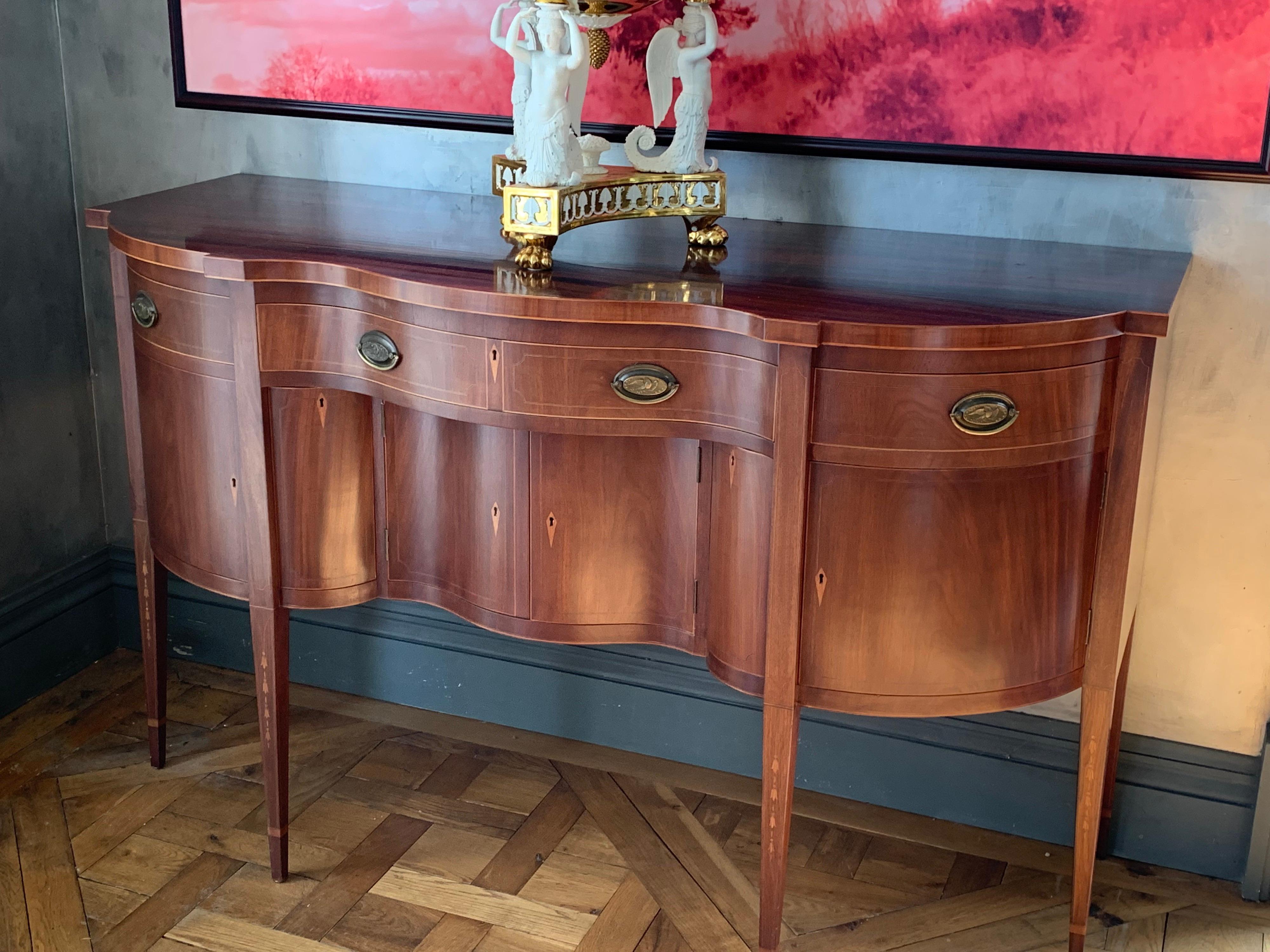 Custom serpentine front mahogany sideboard of highest quality and craftsmanship. Mortice & Tennon construction, dovetailing throughout, band inlays all around and bellflower inlays on the tapered legs. The oval brass pulls have the American Eagle in