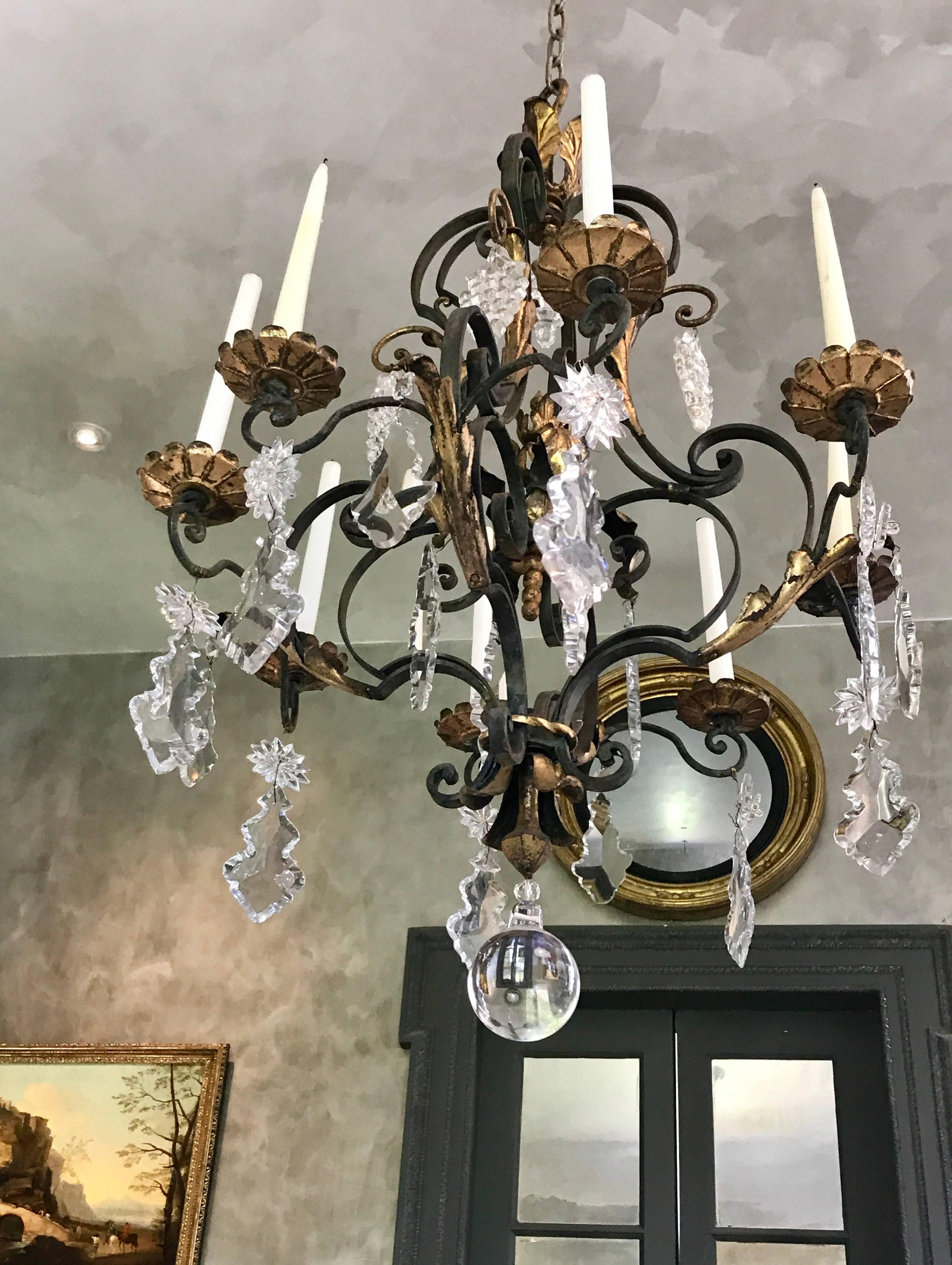 This masterfully crafted Louis XV style eight-arm wrought iron chandelier is a pleasure to look at. 
The lead crystal prisms reflect the warm candle light. 24-karat gold highlights on foliate scrolls and the bobeches give the chandelier