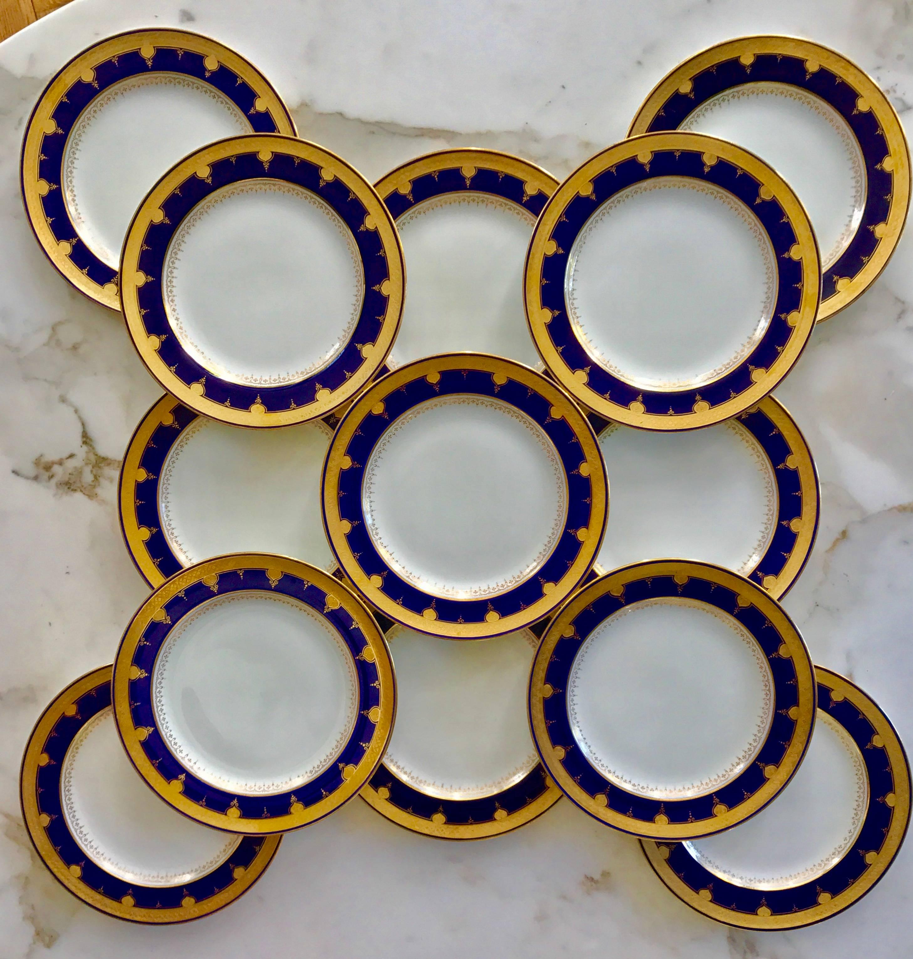 Cet ensemble de 12 belles assiettes à dîner bordées de bleu cobalt et d'or a été produit par Minton et vendu par David Collamore & Co, New York. 
Avec leur croûte dorée légèrement surélevée et leur motif unique, ils attirent tous les regards.
 