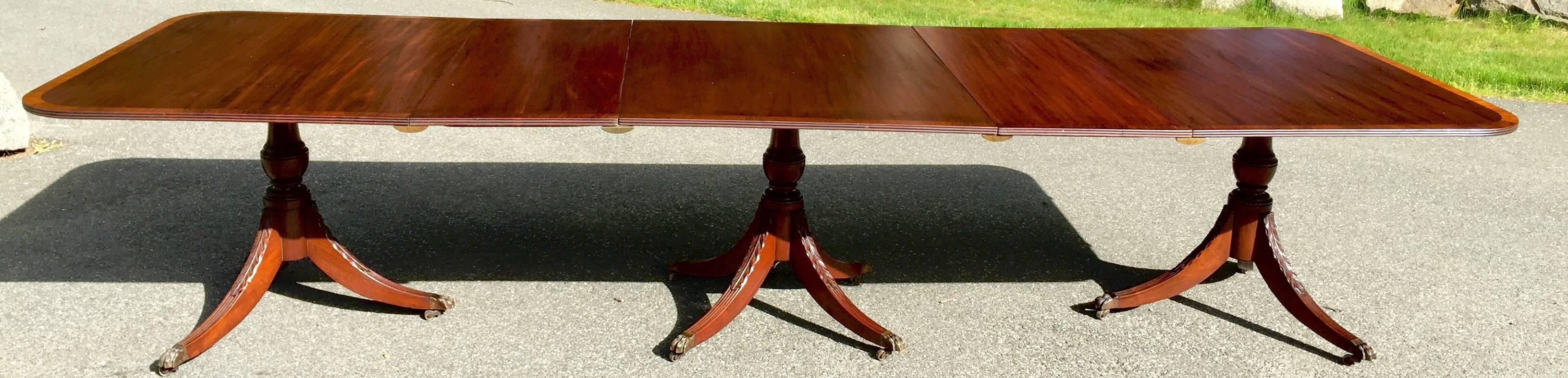 This Regency style 3 Pedestal expansion Dining Table has a stunning solid striped Santo Domingo Mahogany top with a contrasting light banded edge. 
The base consists of three finely carved Duncan Phyfe style pedestals ending in the Classic solid
