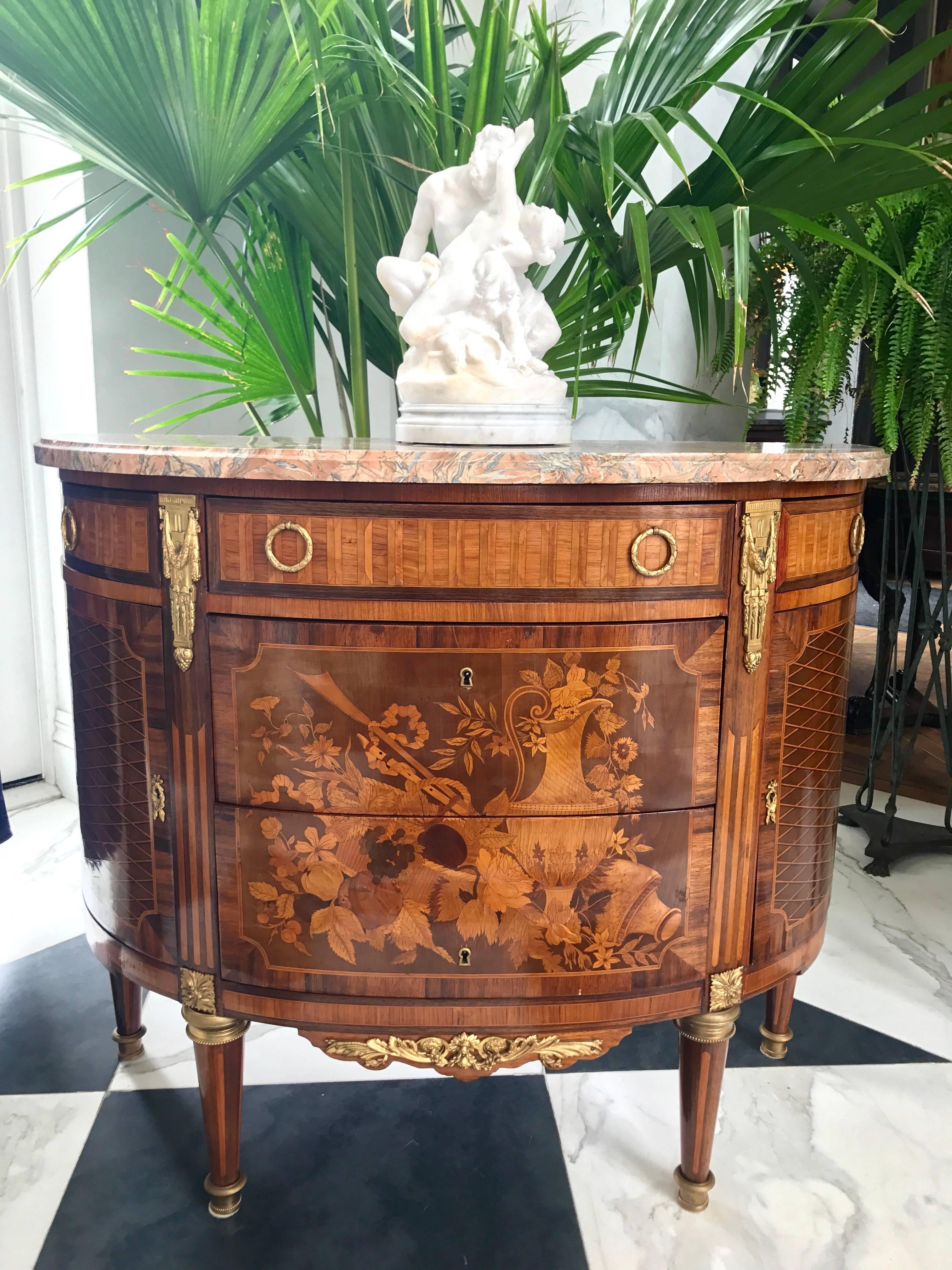 This is an awe dropping Louis XVI style commode displaying the finest craftsmanship in the manner of Charles Topino. The main focus goes to the central drawers, which are elaborately inlaid with multiple wood varieties depicting a ewer, an urn and