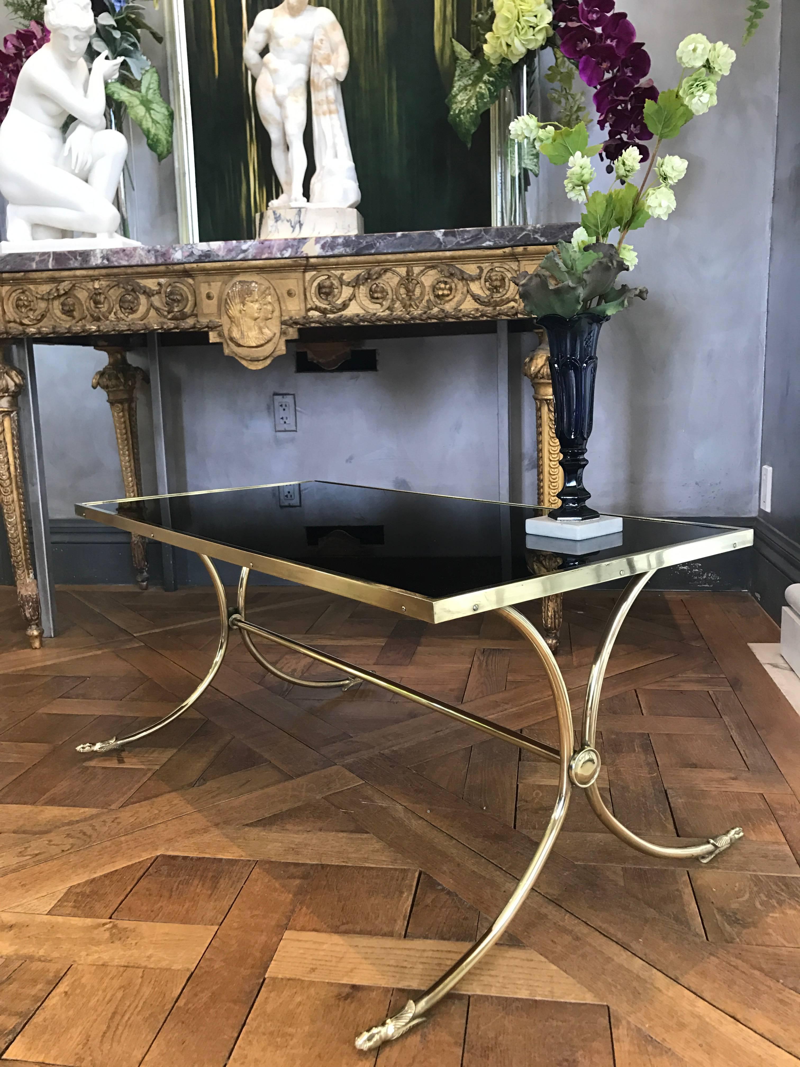 Cette élégante table basse française de style néoclassique Jansen est fabriquée à partir d'une base en laiton massif et polie à un haut degré d'éclat. Le plateau en verre noir est entouré d'un cadre en laiton, le verre est en excellent état. 
Les