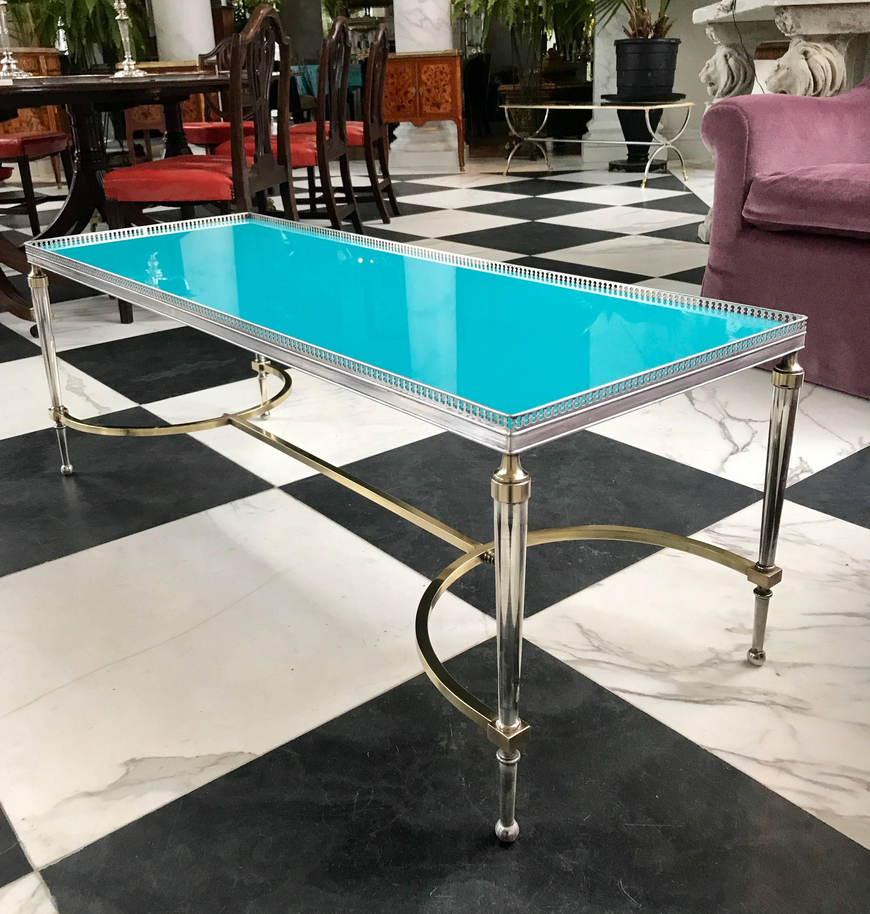 This is a rare and detailed Maison Jansen Style coffee table manufactured in the 1960s in France.
The legs and gallery top are made of solid brass the frame work is polished aluminum. 
The beautyful detailed gallery and the replaced colored glass