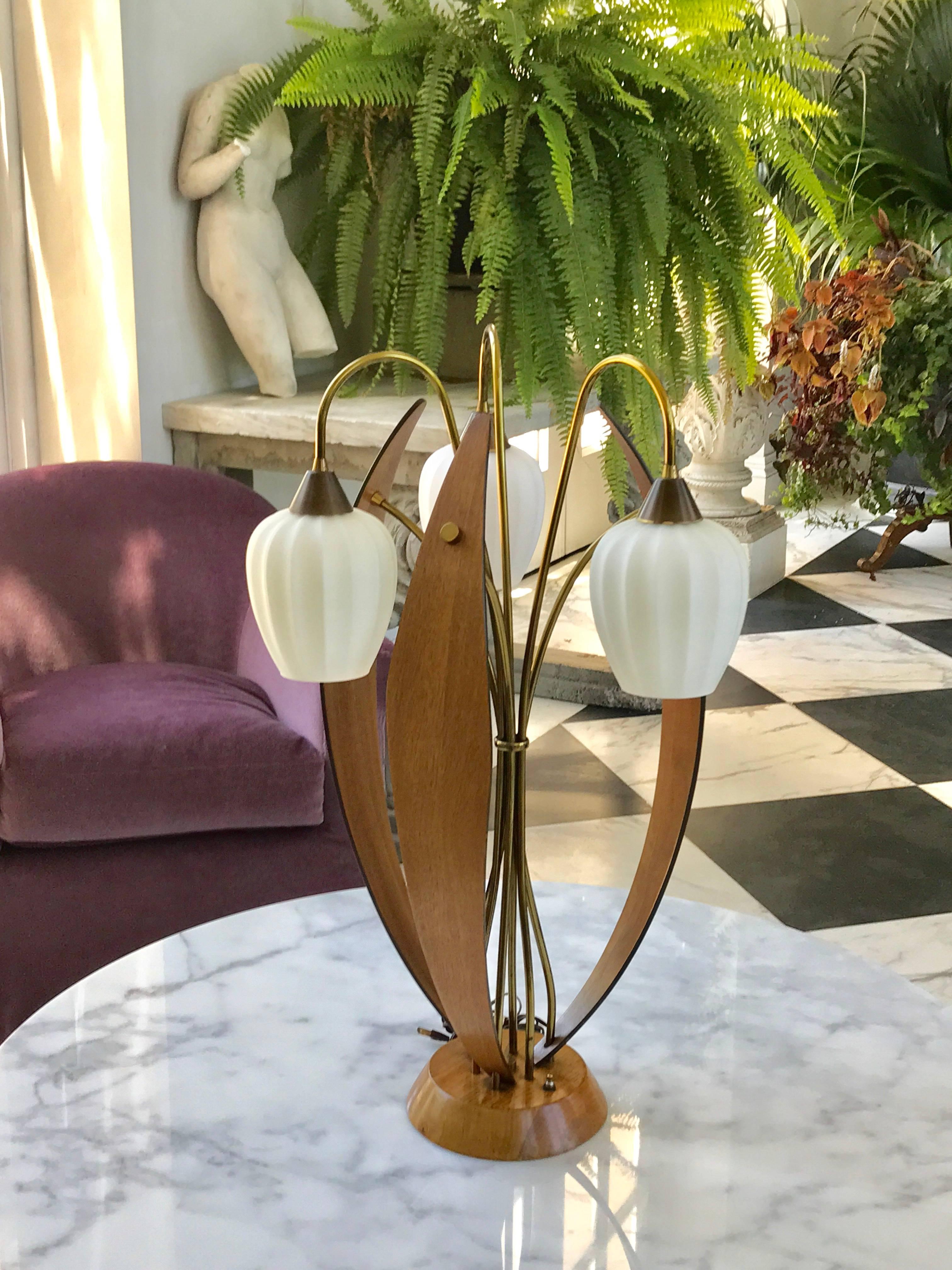 This very unique large-scale brass and walnut table lamp.
It has three frosted glass shades rising out of the central shaft like flowers bound by a brass ring in the middle.
Between them are wooden walnut “sails”.
American made, circa 1970.