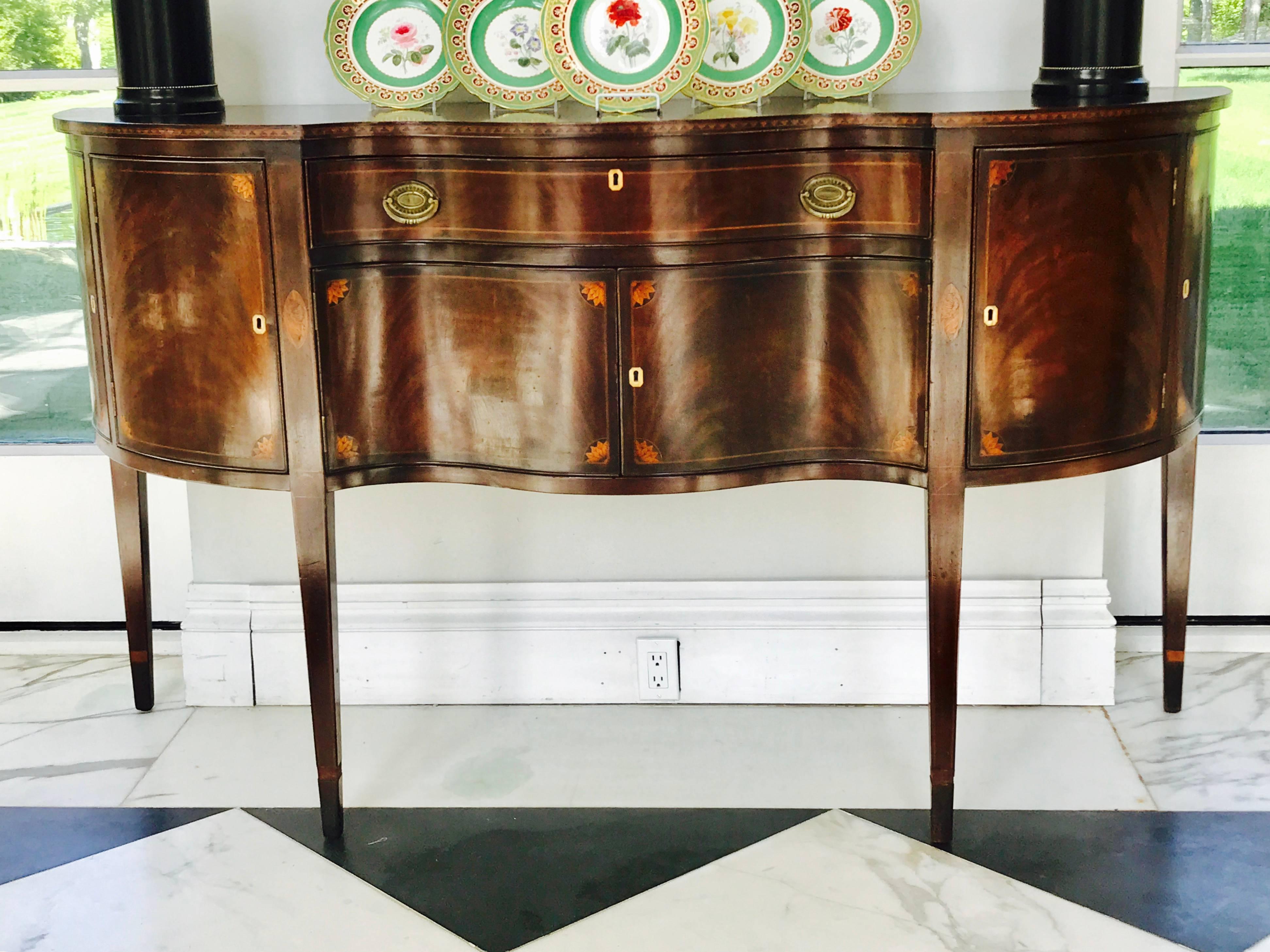 This beautiful serpentine front Hepplewhite sideboard was custom-made in Baltimore in the late 19th century using the finest crotch grain Mahogany veneer on the front and sides and a solid mahogany top.
Intricate foliate and shell motif inlays in