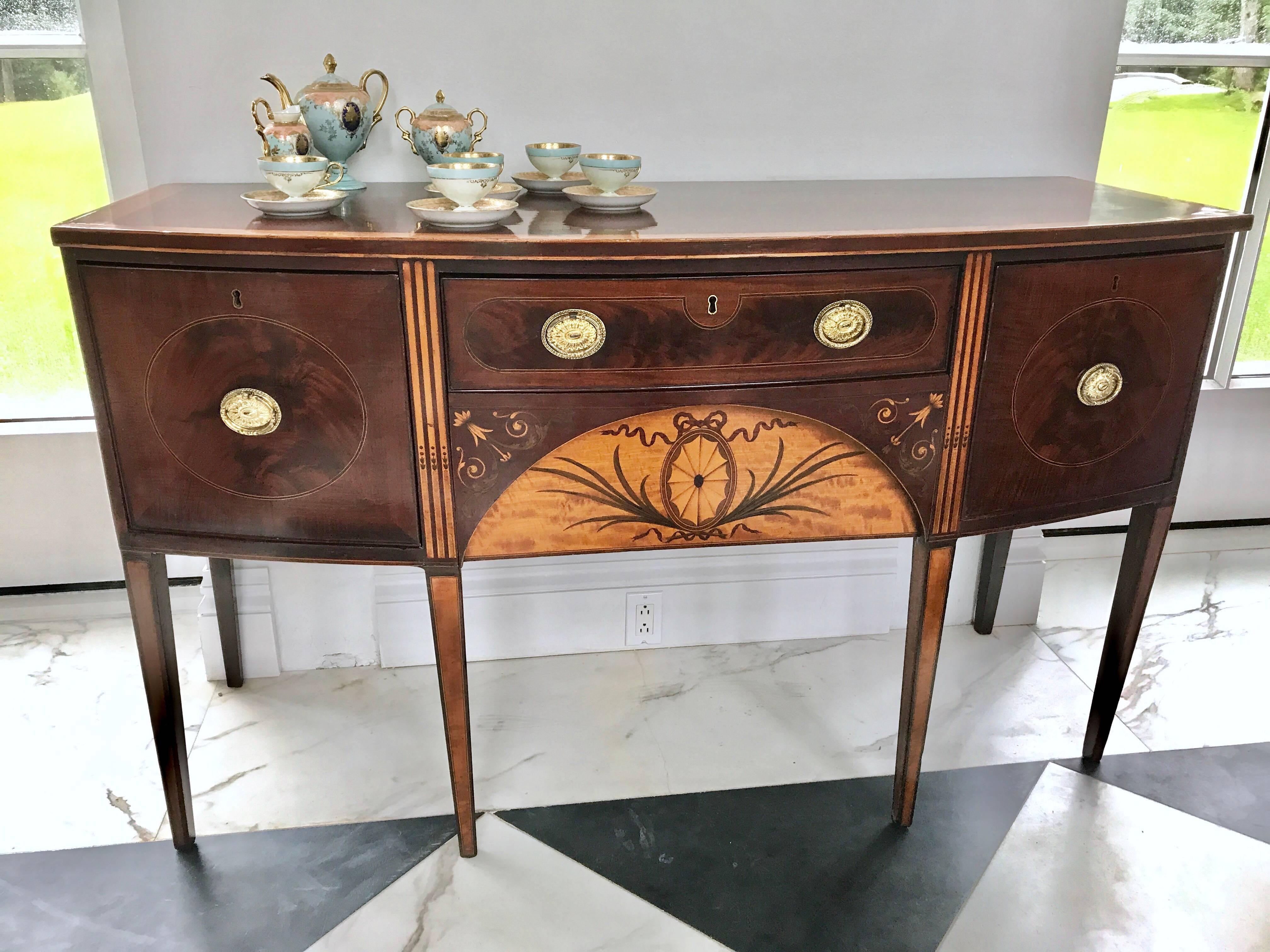 A fine Hepplewhite period sideboard, attributed to one of the finest English furniture makers Mayhew & Ince.
It is elaborately inlaid with contrasting satinwood.
The central arch is inlaid with kingwood, tulipwood and olivewood palms, ribbons and