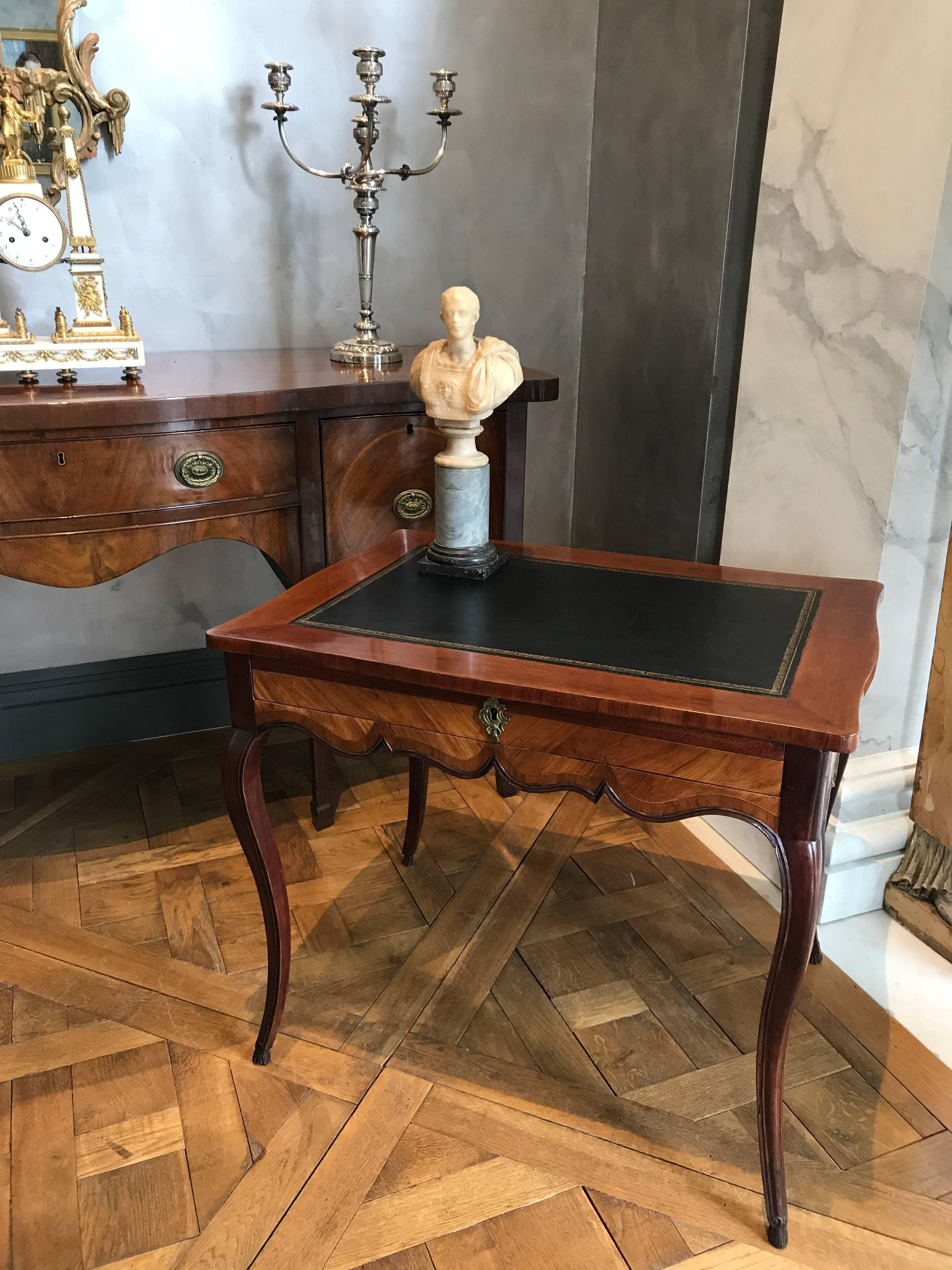 This elegant Gustavian writing table was made in the late 18th century out of kingwood and tulipwood with solid mahogany curved legs ending in hove feet. The apron is scalloped and has a single large drawer in the front. The black tooled leather top