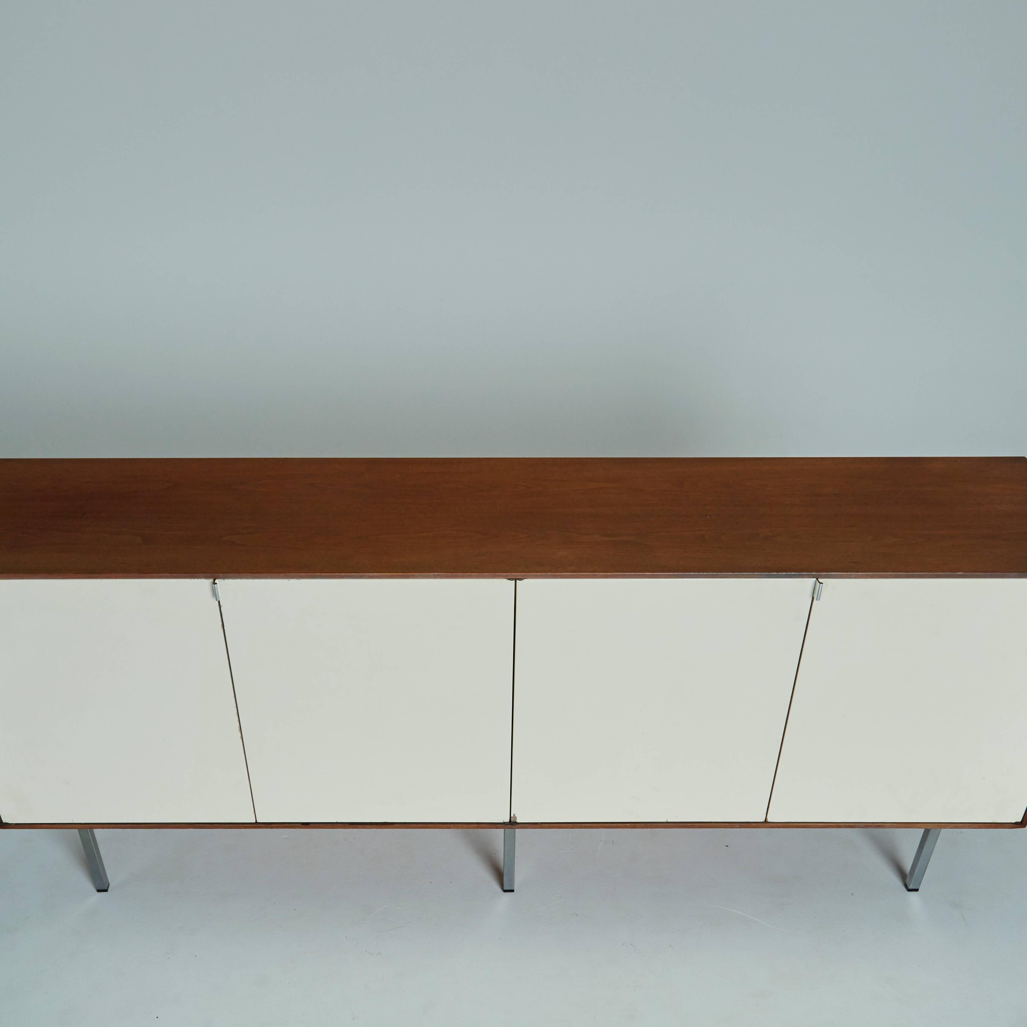 Created by Florence Knoll, circa 1950s, this storage cabinet is exemplary of her Minimalist and utilitarian design values. The walnut body of this credenza is enclosed by four white lacquered steel cabinet doors. The birch interior features open