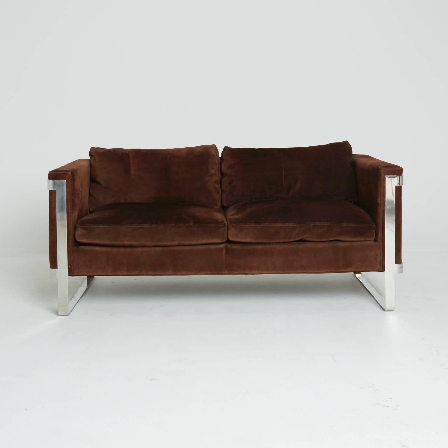 A two-seat settee with luxuriously rich brown suede upholstery that seems to float within the flat bar chrome frame that wraps around the edges. While this loveseat was created in the style of Milo Baughman, it also pays a very strong homage to the