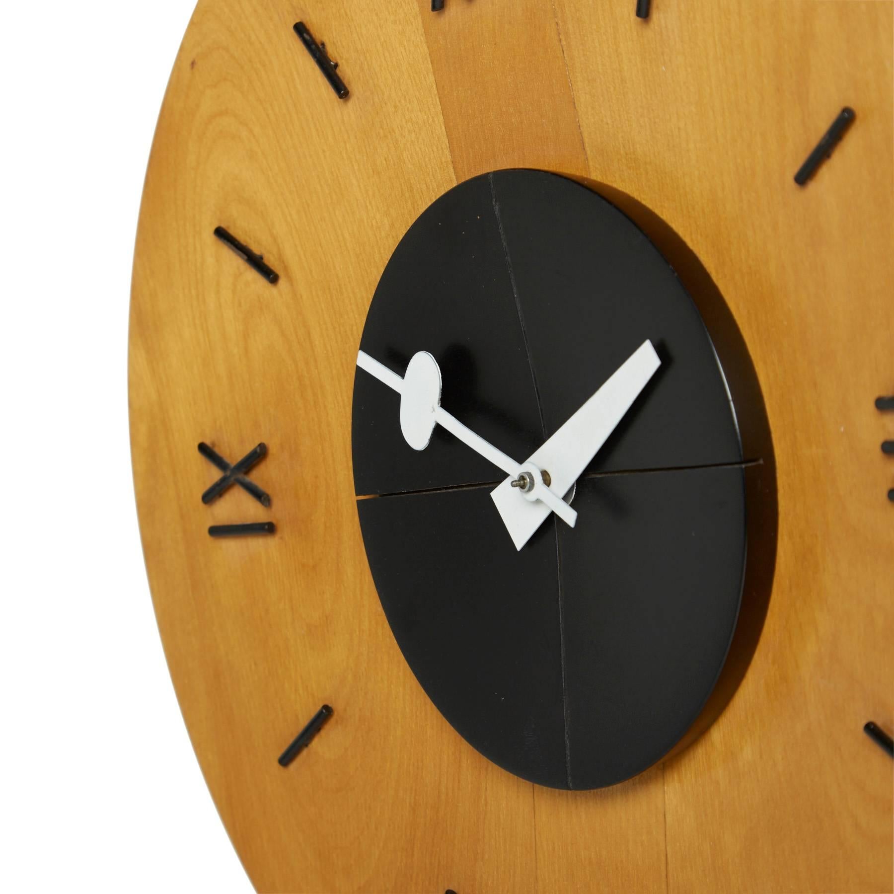 This modernist wall clock is an original design by George Nelson for Howard Miller. Roman numerals and lined notches mark the round light birch wood face of the clock. From the black platform in the center are the Classic, atomic white and red