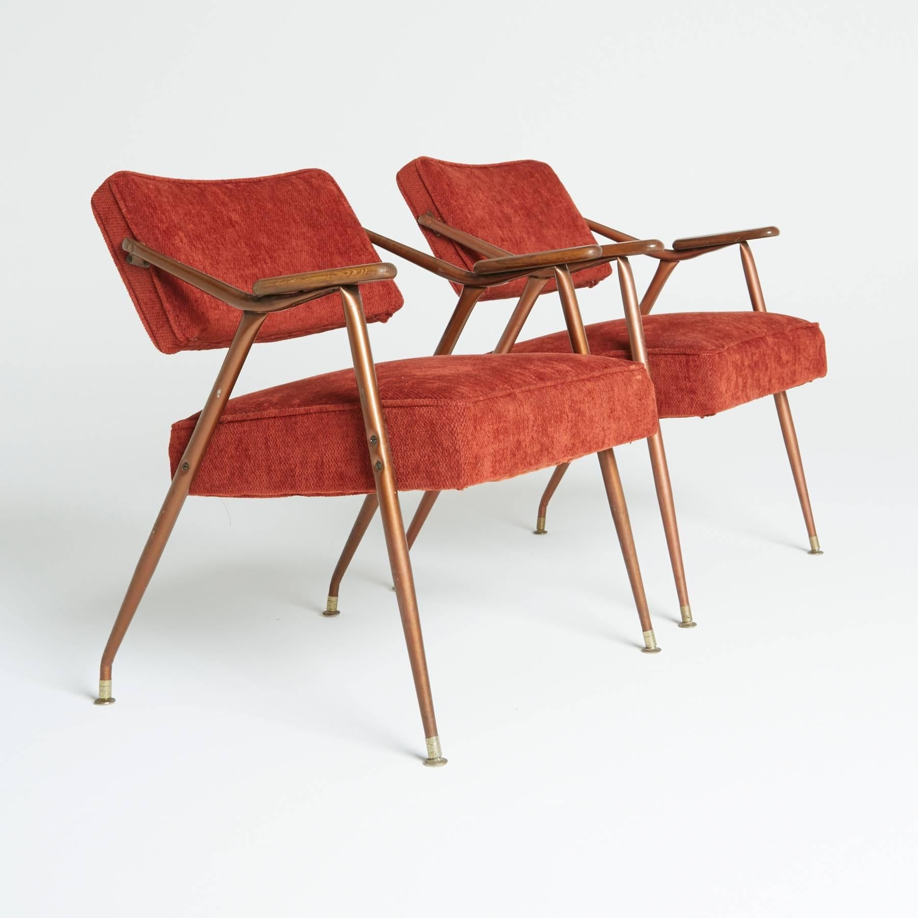 These Mid-Century armchairs have the lean of a lounge chair and the poise to command attention. Slanted tubular metal frames have wooden arm rests and are capped with Classic sliders at the feet. The deep red chenille upholstery has a dynamic sheen