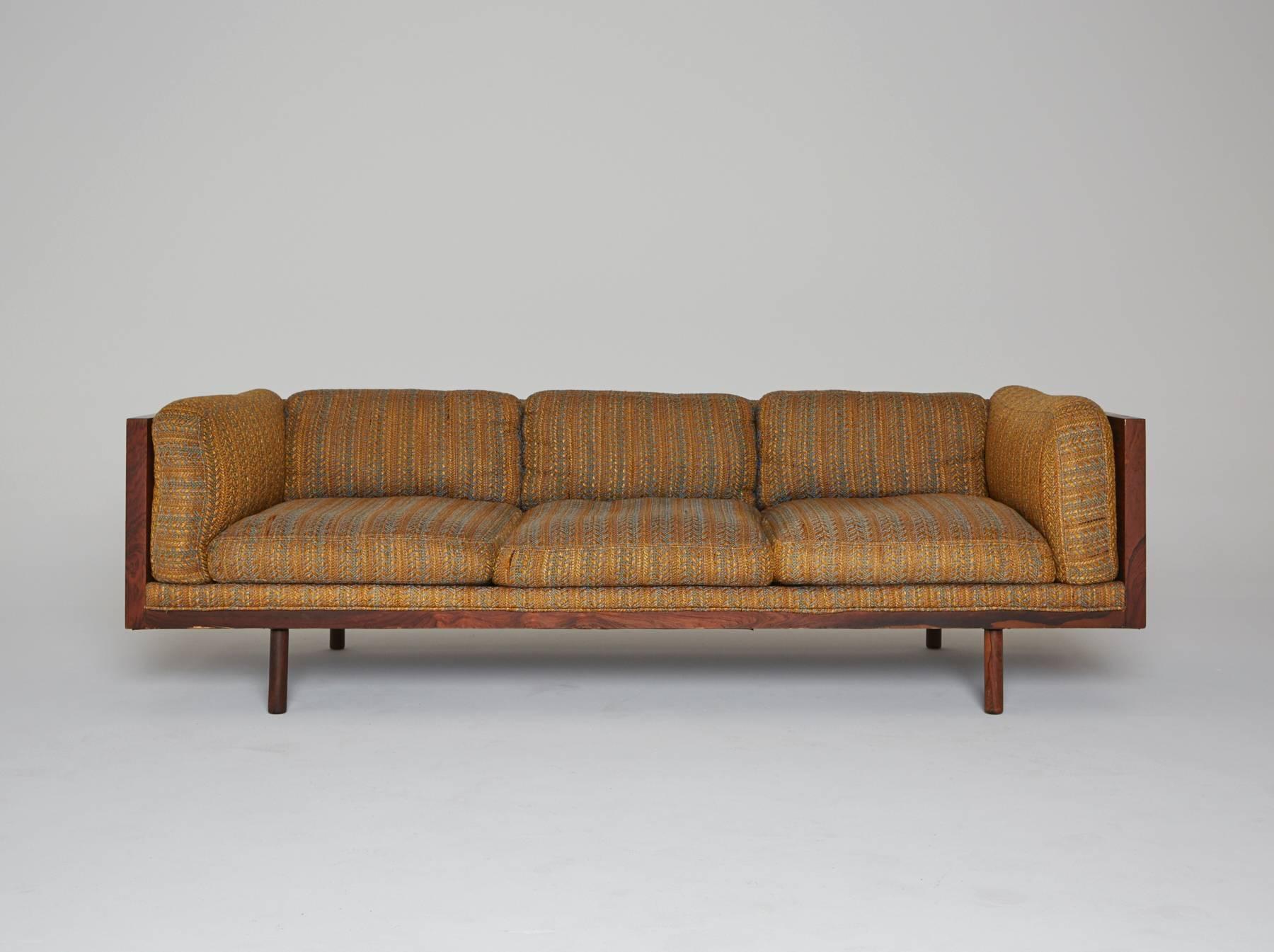 A coveted 1960s sofa designed by Milo Baughman for Thayer Coggin. Luxurious rosewood provides a beautiful frame encasement. This regal sofa appears to levitate, as it is elevated onto four wooden peg legs. The gold, woven upholstery has great
