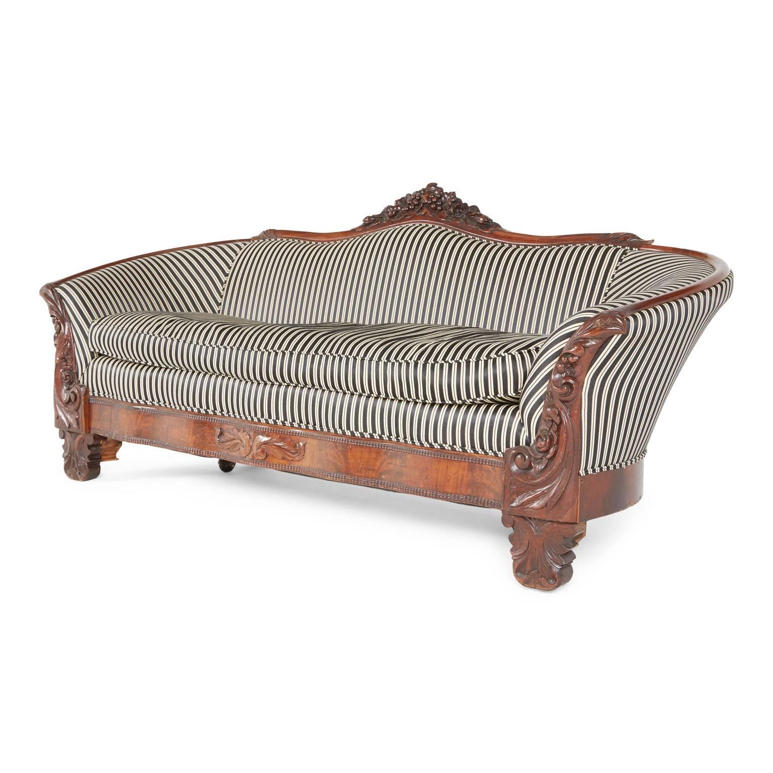 This plush and comfortable Victorian Rococo Revival sofa from the late 1800s displays an amusing modern twist on a period style. The curved delineation fabricated from a solid walnut frame with opulent carvings on the center back and foot, as well
