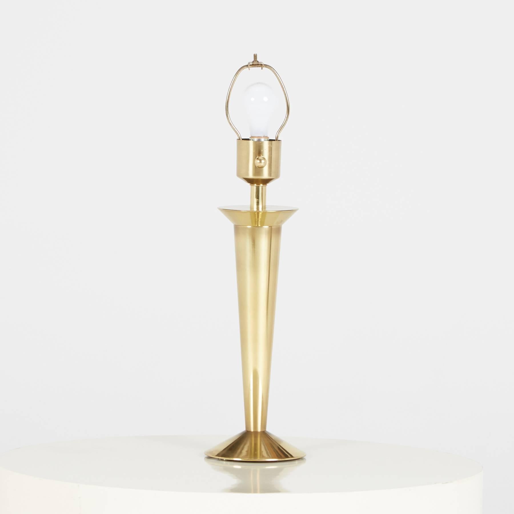 Sleek pair of Hollywood Regency, Art Deco Revival style brass table lamps with white conical shades. Featuring a gleaming brass Silhouette, which when illuminated emanates a dazzling reflection, creating a warm glow. These lamps include round