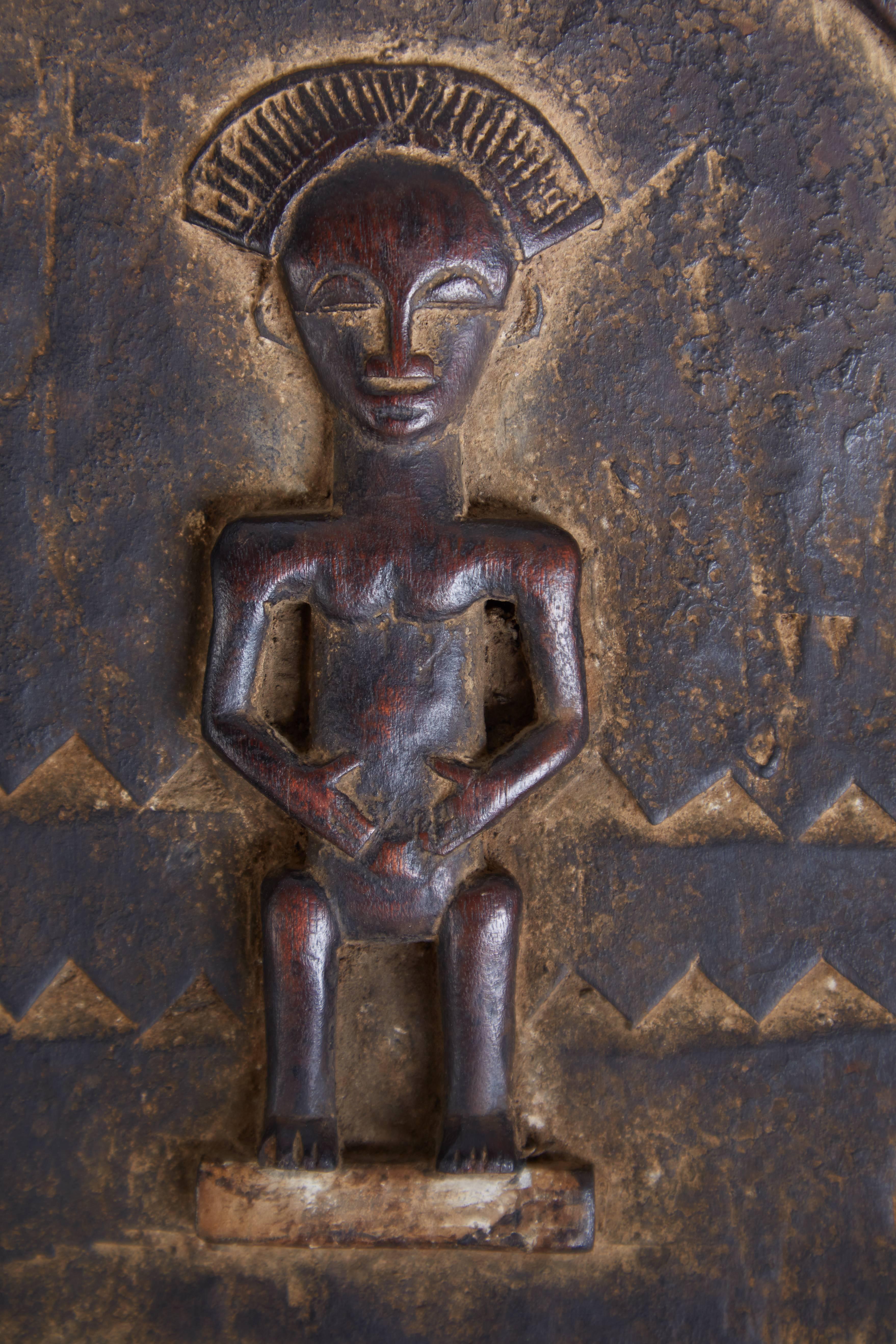 Petite decorative Ivory Coast carved granary door featuring an African figure, snake and fierce looking predatory animal below. There is also a repeating small chevron pattern around the border and across the center and two spokes at one end where