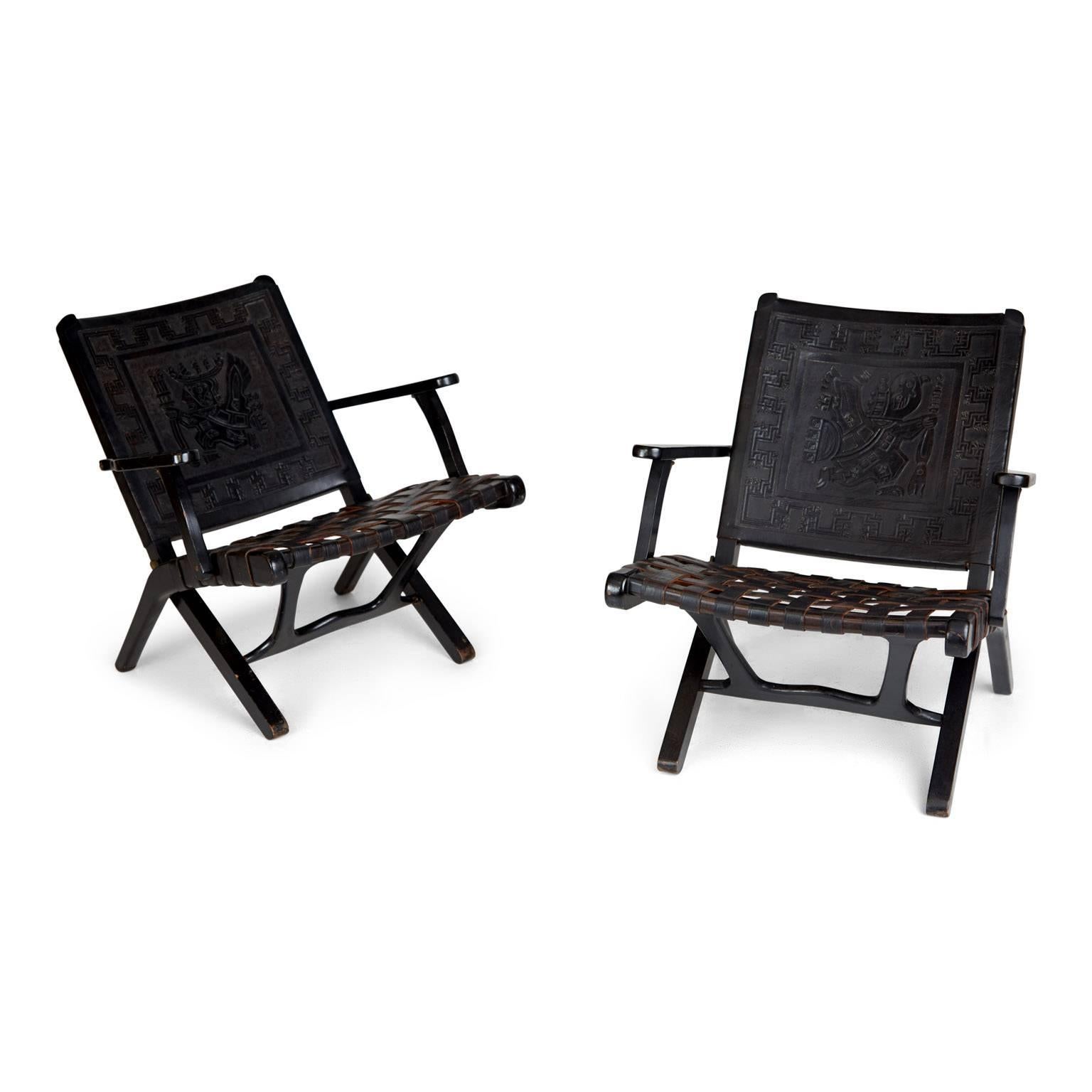 Pair of two exquisitely crafted black leather Peruvian folding chairs. Each chair features a tooled leather backrest with a different motif in the centre, surrounded by an ornate border and the seats are fabricated from woven strips of leather.
The
