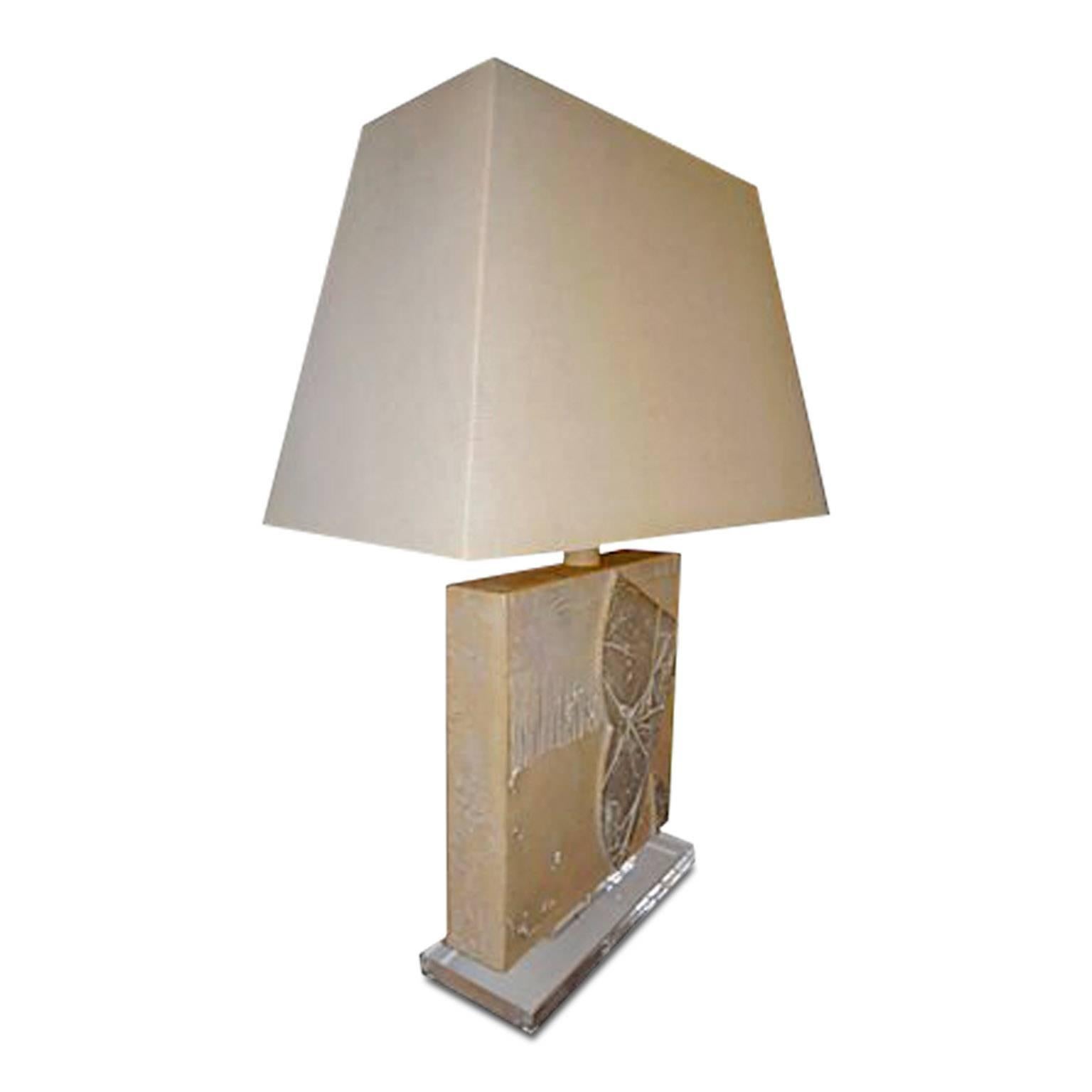 Mid-Century Modern table lamp decorated to give the appearance of carved engraved clay slabs atop of a Lucite base which are contrastive on the front and back. The simple, clean shape its calm, neutral colors would work with a number of interiors. A
