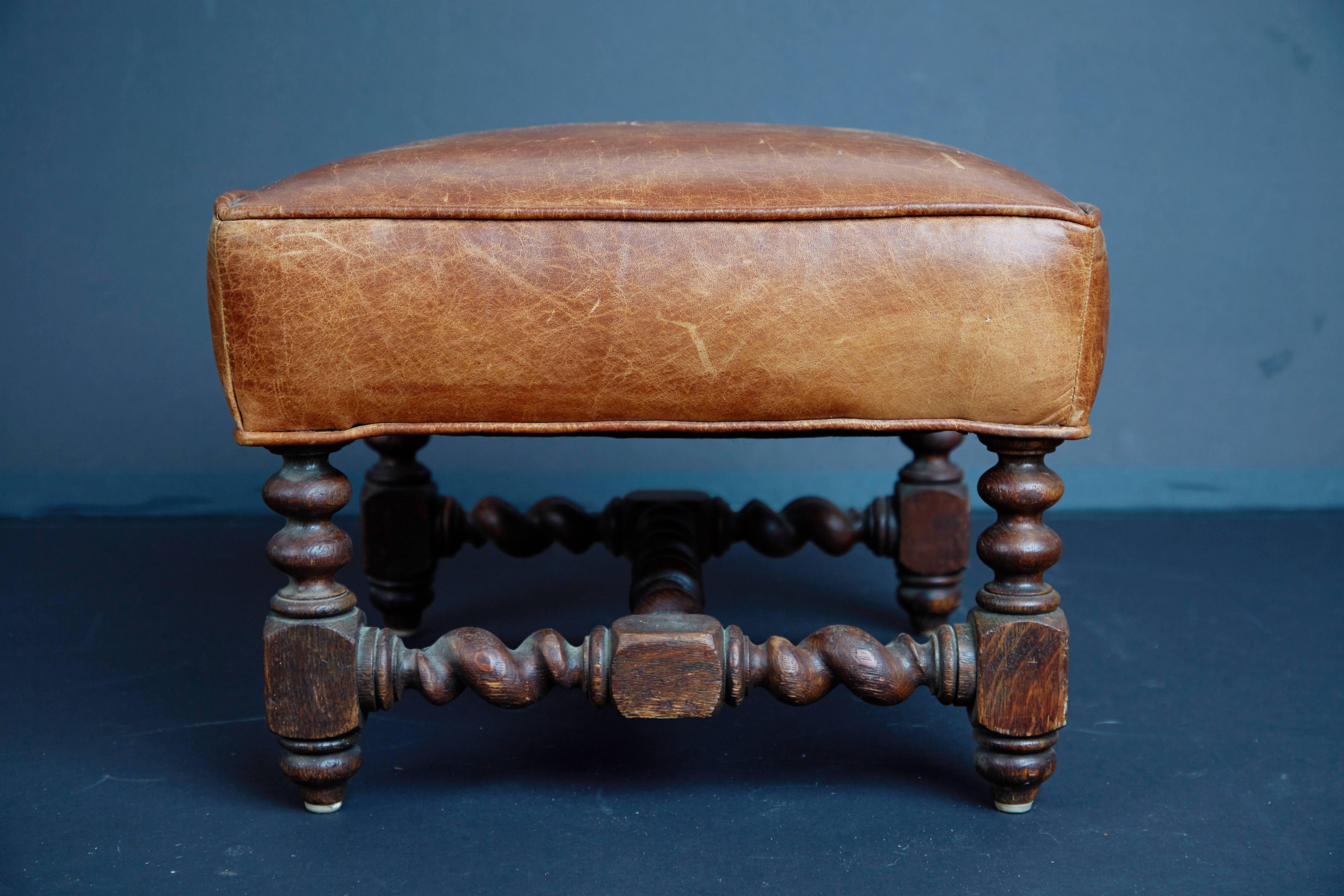 Beautifully crafted Spanish Baroque style footstool or ottoman featuring tan leather upholstery and turned wood base finished in a rich dark stain. The original leather upholstery has developed an admirable patina. These traces of age and use bring