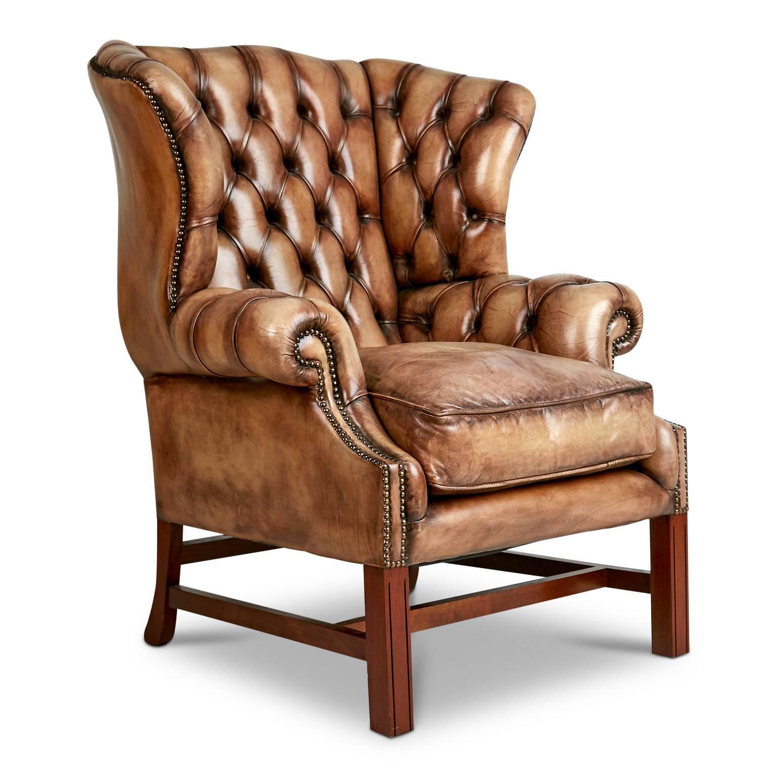 Add a touch of nobility to your space with this George III style English tufted leather wingback fireplace arm chair. This handsome Chesterfield lounge chair is upholstered in a quality medium tone brown leather which has a slightly distressed look