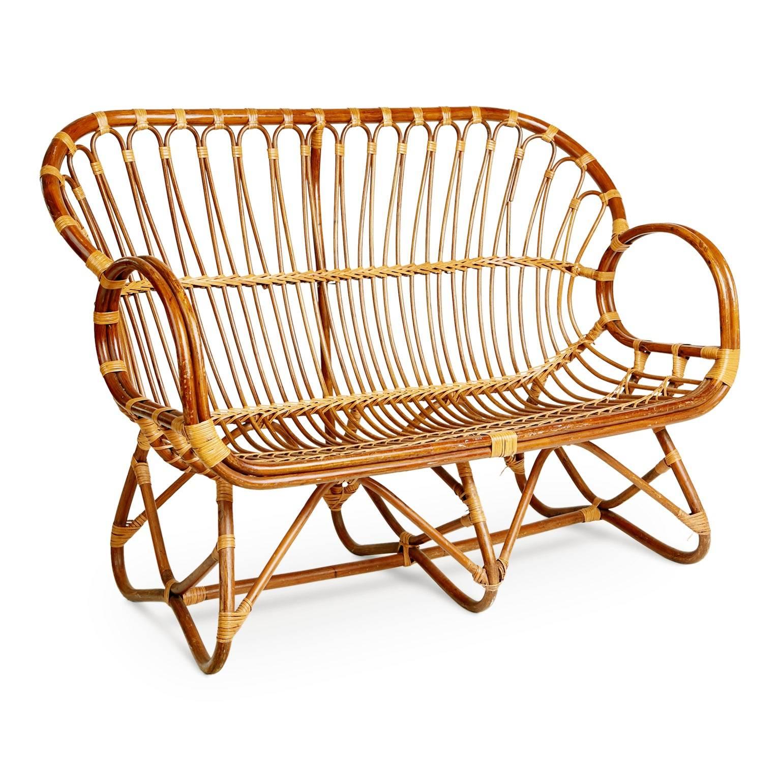 Possessing an amazing silhouette, this elegantly executed settee in the style of Franco Albini was fabricated from bent bamboo and tied off with cane accents forming an arched seat and with scrolled arms and integral twisted base. The simplicity of