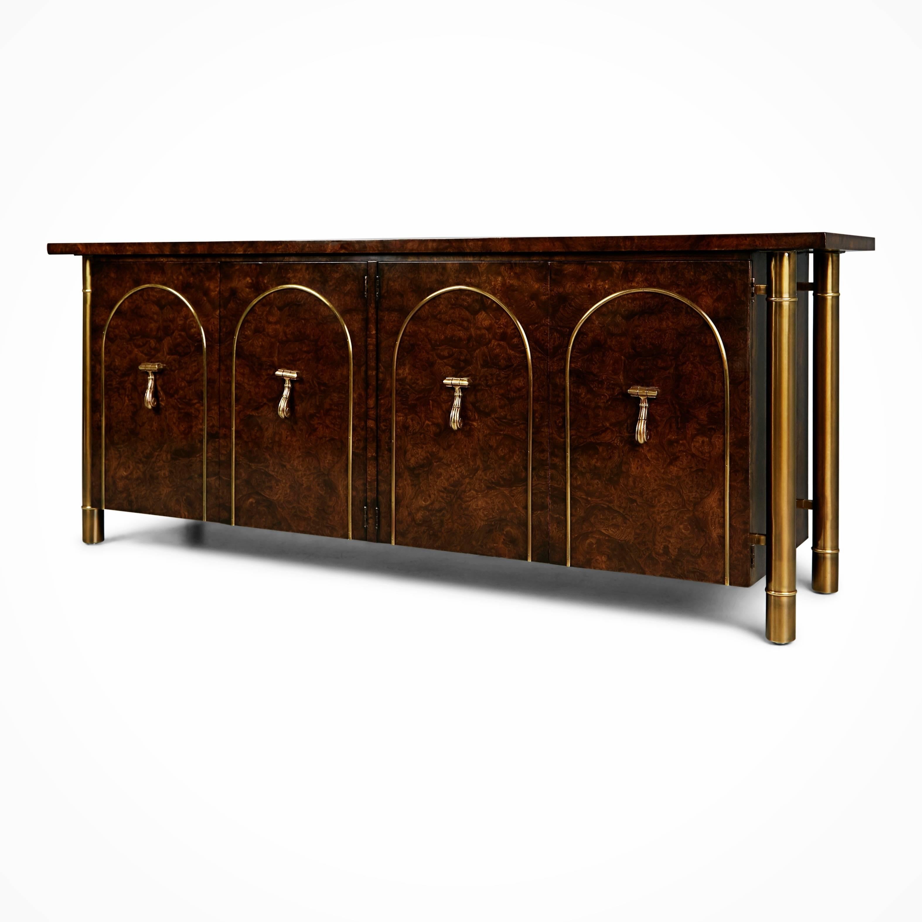 An incredibly high quality and hefty credenza, in excellent showroom condition, by William Doezema for Mastercraft features a burl wood finish with brass cylindrical legs running the length of the cabinet from under the top down to the floor. There