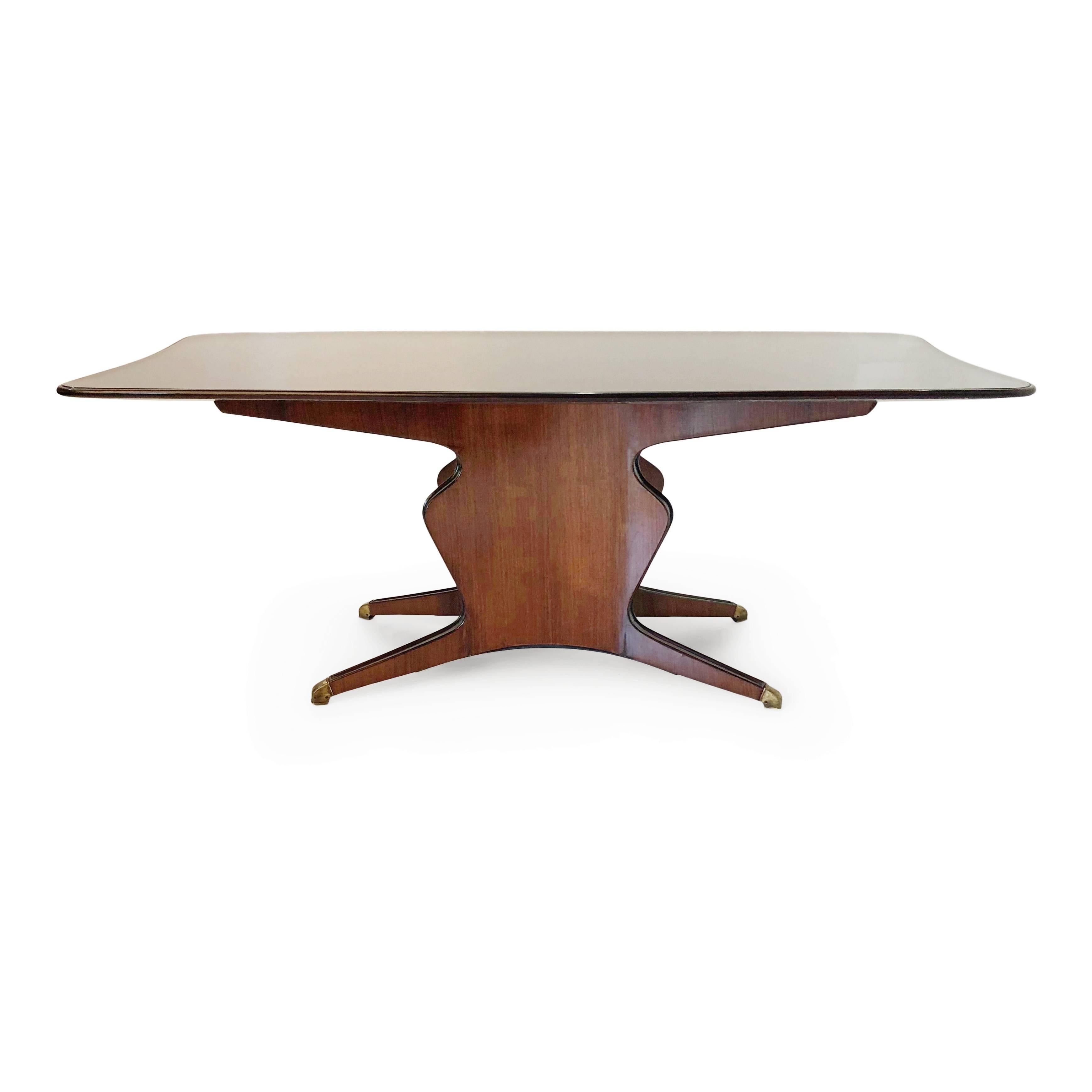 Expansive Italian dining table in the style of Osvaldo Borsani. This handsome table is fabricated from a beautiful bold-grained rosewood with sculptural base and brass sabots. The broad top has a dark colored glass surface which reflects the light.