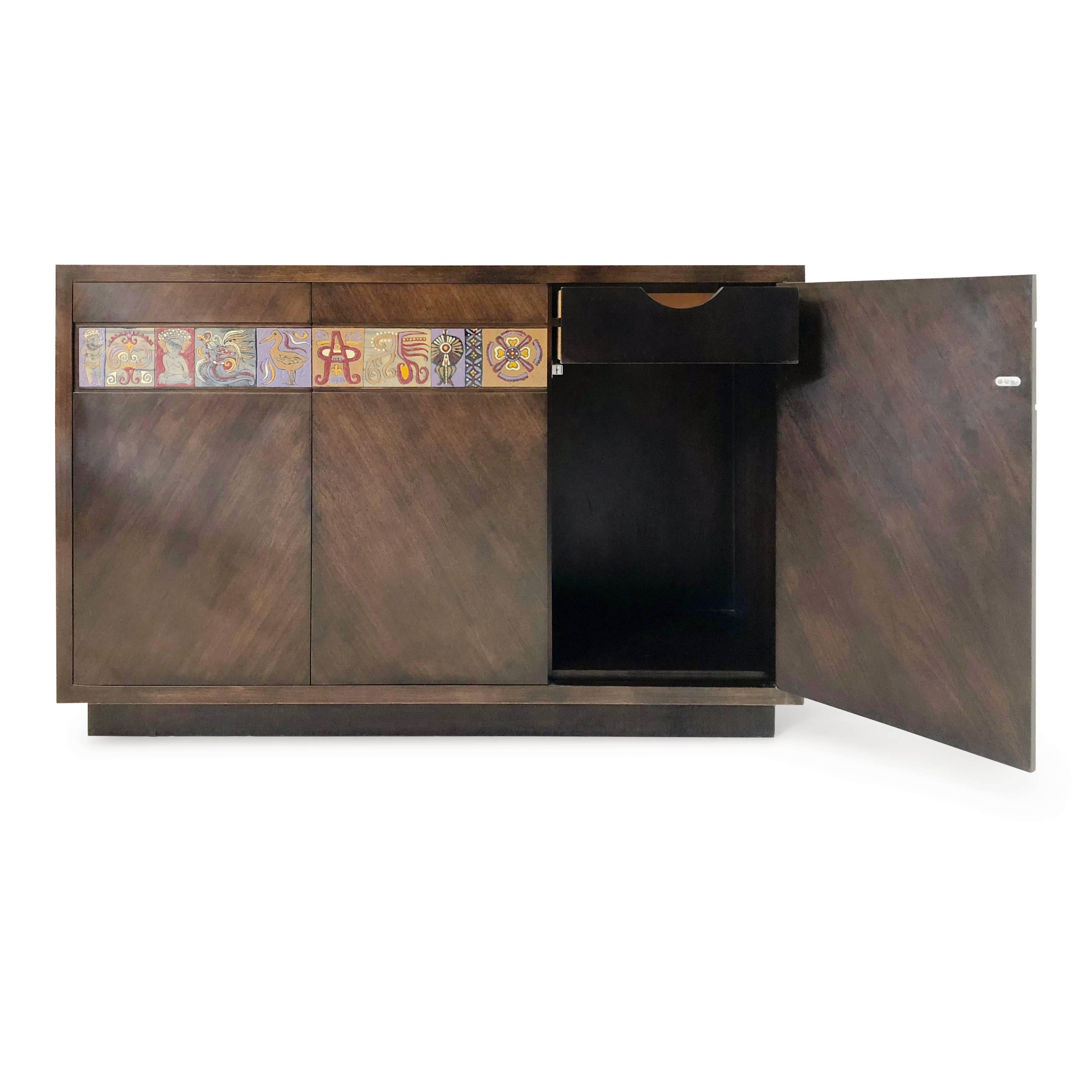 Beautifully constructed Mexican modernist credenza decorated with enameled tile inserts. These colorful tiles have been hand-painted with Primitive motifs and encased in a strip along the top portion of the credenza. The doors of the cabinet have
